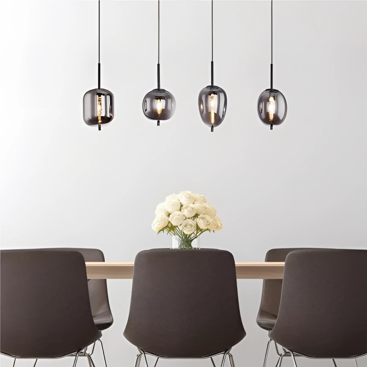 Modern industrial glass pendant lights in bronze finish hanging above a dining table, complementing the white and black interior decor with a touch of greenery from the plant.