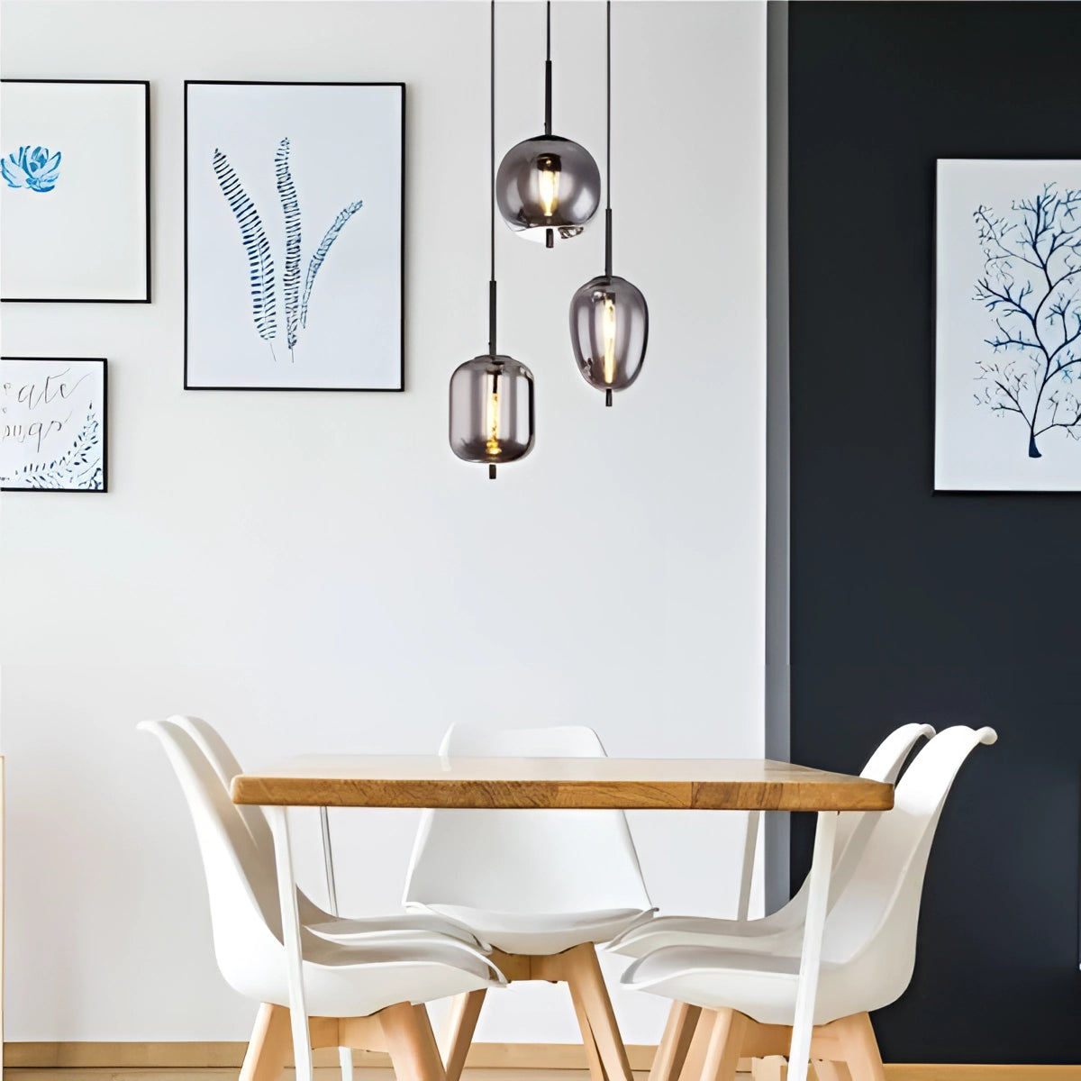 Modern industrial glass pendant lights with bronze finish hanging above a dining table with white chairs and wooden elements.