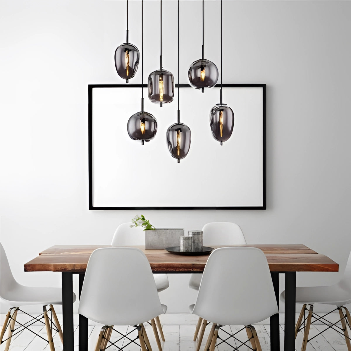 Modern industrial glass pendant lights with bronze finish hanging above a contemporary dining table with wooden furniture and white decor.