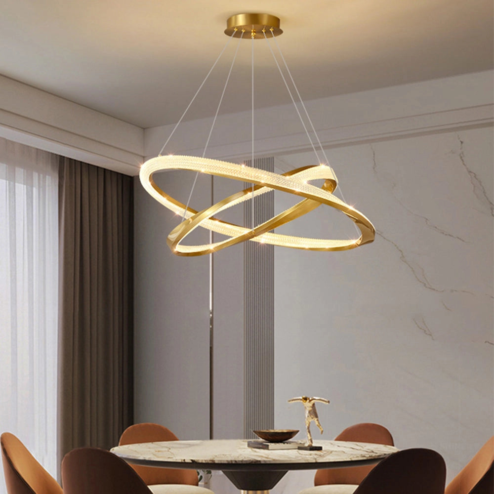 Modern LED chandelier in a golden minimalist design hanging from the ceiling, illuminating a contemporary interior space featuring a wooden table and chairs, with yellow curtains and wooden flooring.