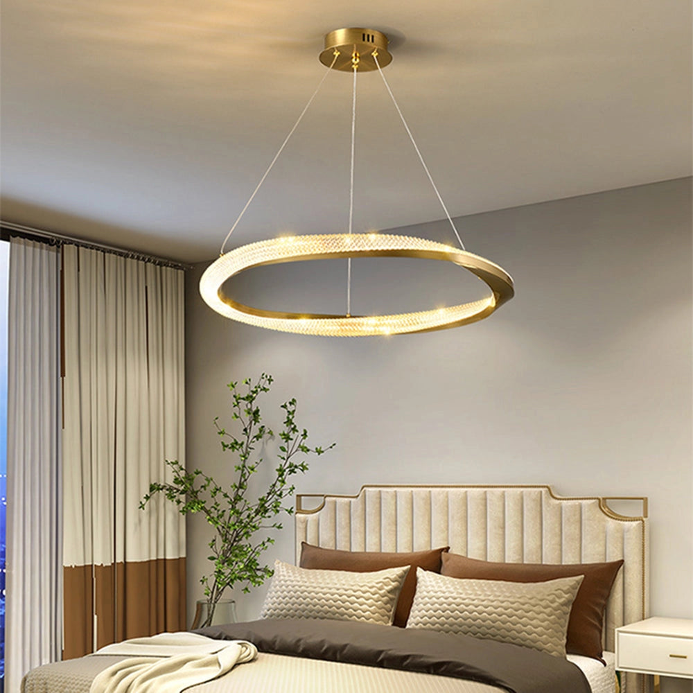 Modern LED chandelier with a golden minimalist pendant light design, measuring 23.6 inches, hanging in a stylish interior setting. The room features warm wooden accents, lush green plants, textile elements, and soft curtains, creating a cozy and elegant atmosphere.