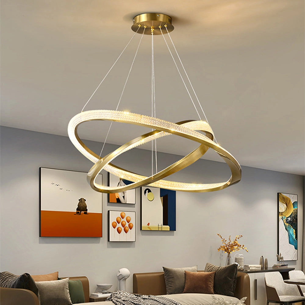 Modern LED chandelier with a golden minimalist pendant light design, hanging elegantly in a stylish living room featuring a couch, picture frame, and a table, accented by cozy furnishings and plants.