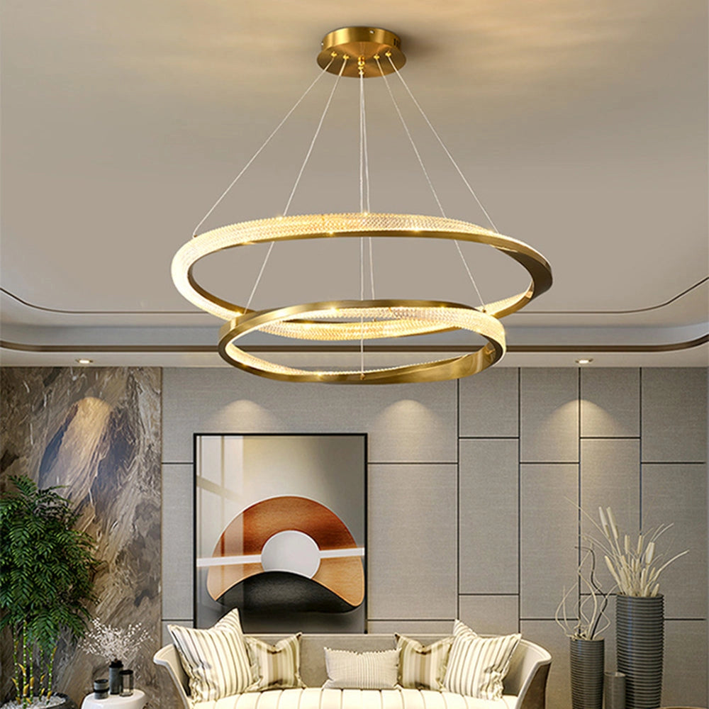 Modern LED chandelier with a golden minimalist design featuring two intertwined rings measuring 23.6 inches and 31.5 inches, elegantly hanging in a contemporary living room setting with wooden floor and decorative plants.