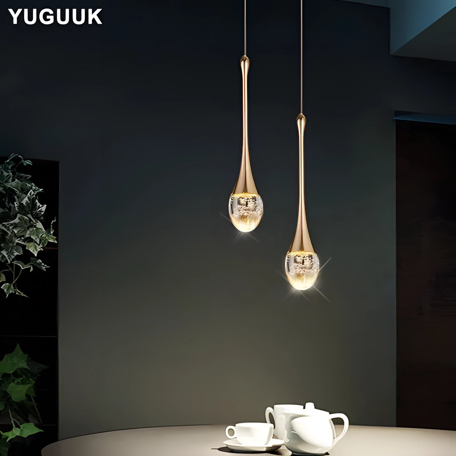 Modern LED gold teardrop pendant lights hanging over a stylish dining table set with white and black tableware, including coffee cups, in a tastefully designed interior.