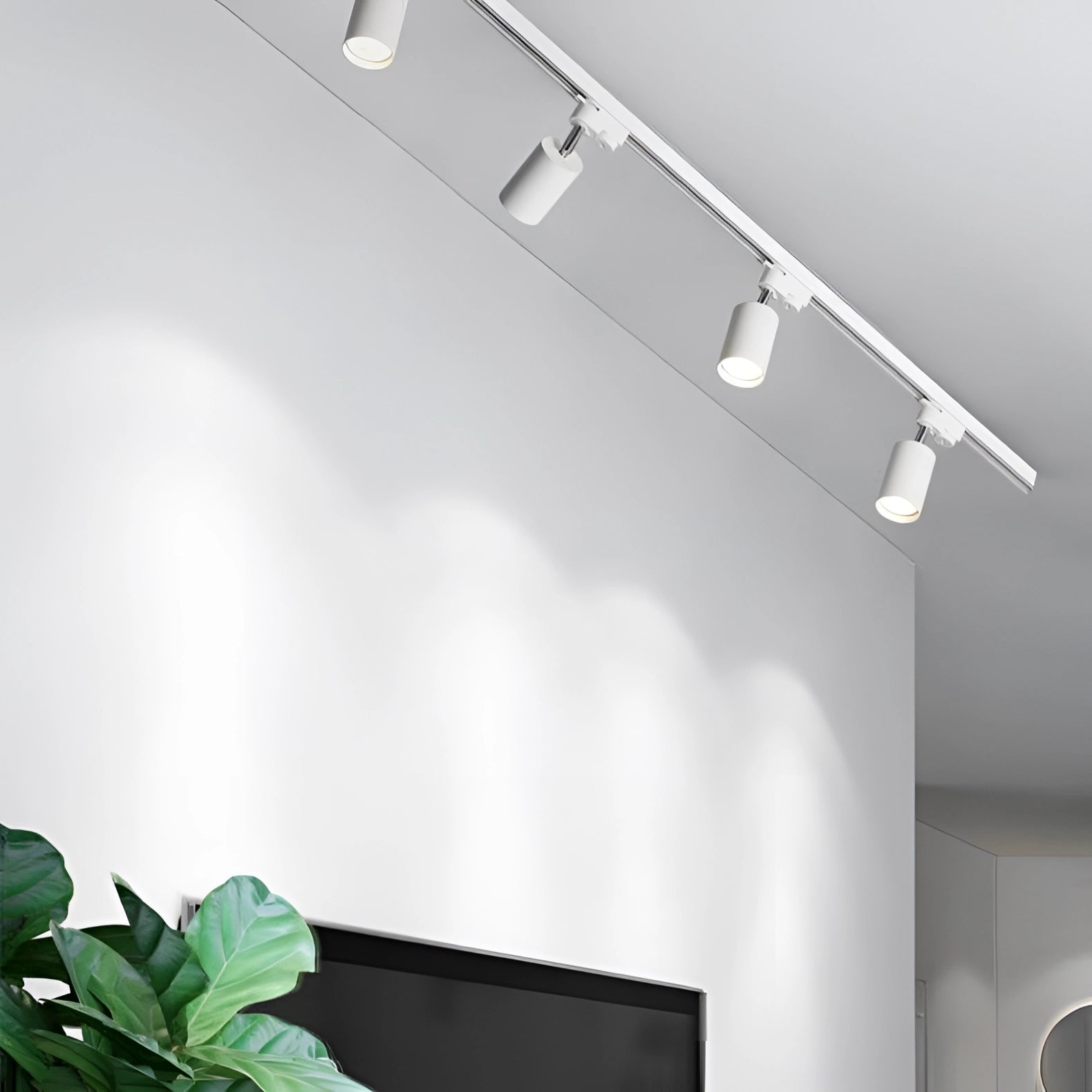 Modern LED track lighting fixture with four adjustable spotlights in a sleek white finish, mounted on a 59.06-inch spur. The lighting system is installed on the ceiling, illuminating the space with a contemporary design. A white wall and a potted plant are visible in the background, showcasing a harmonious blend of functionality and style.