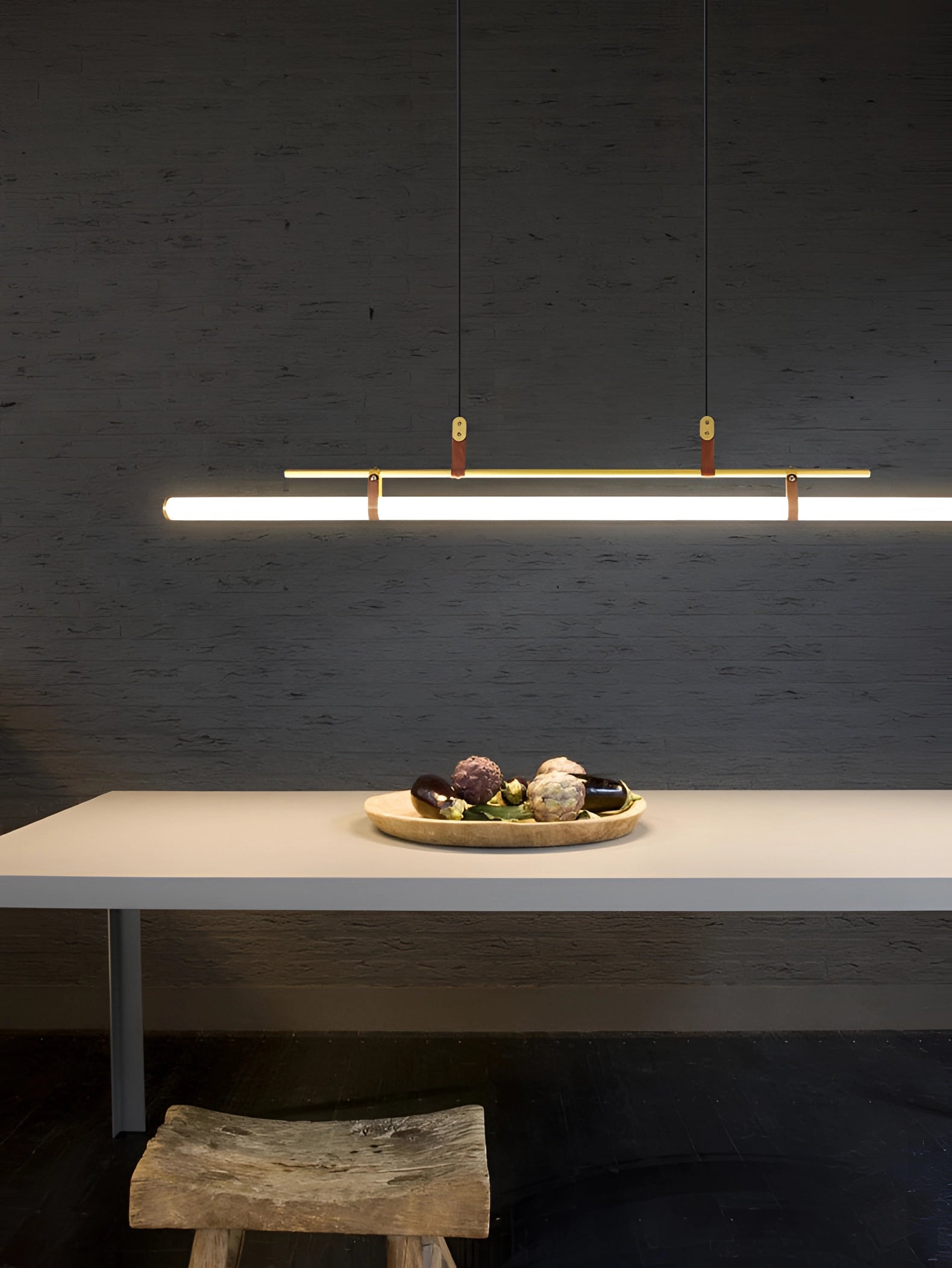 Modern LED tube pendant light hanging above a minimalist kitchen and dining room setting with wooden flooring and tableware on the table.