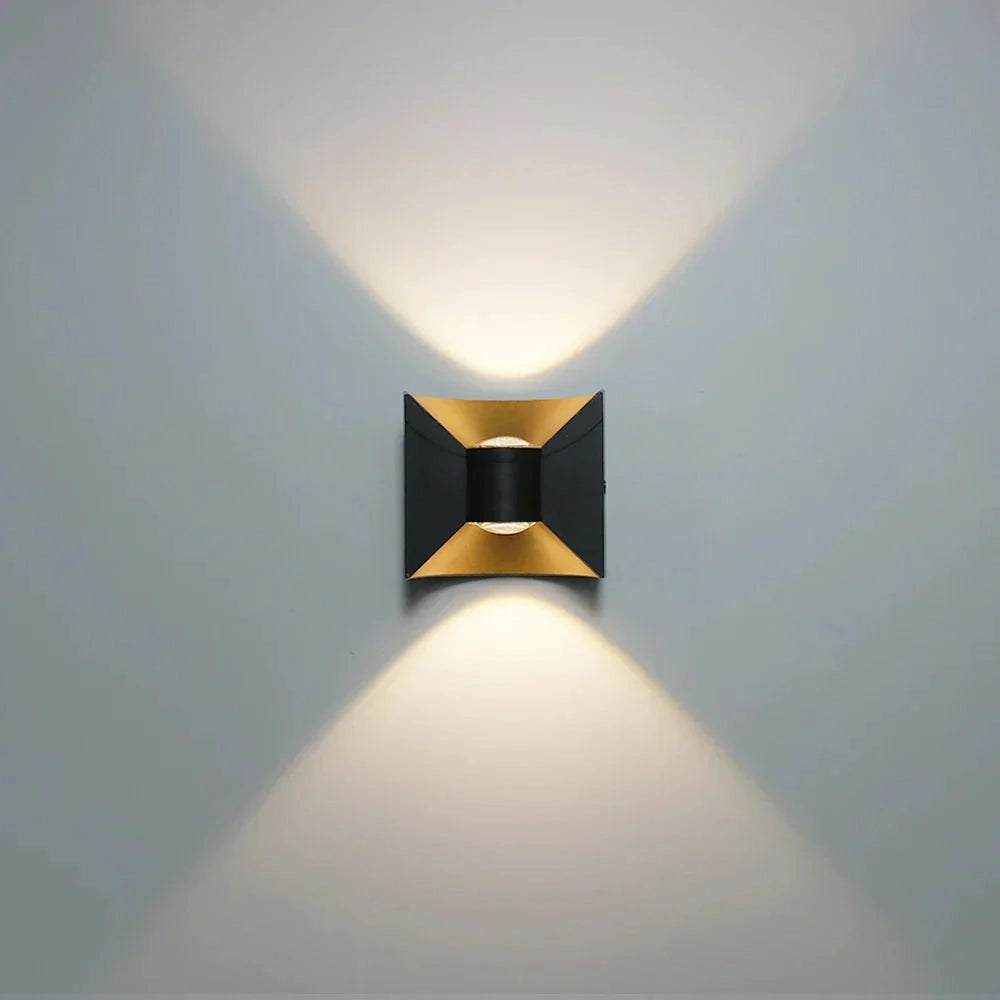 Modern LED wall sconce with a geometric design in black and gold, featuring cool white light, mounted on a wall.