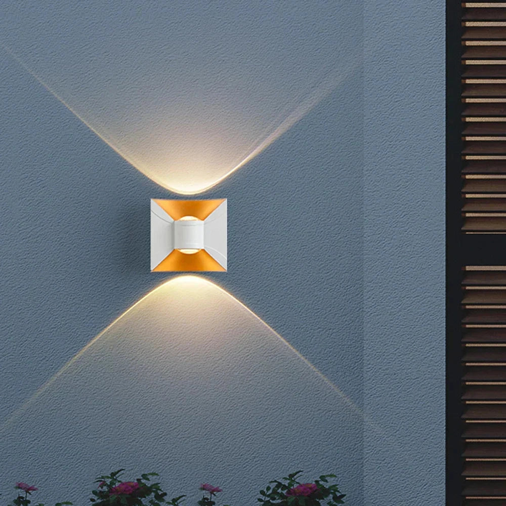 Modern LED wall sconce with a black and gold geometric design, featuring a rectangular shape and symmetrical lines, emitting a soft light.