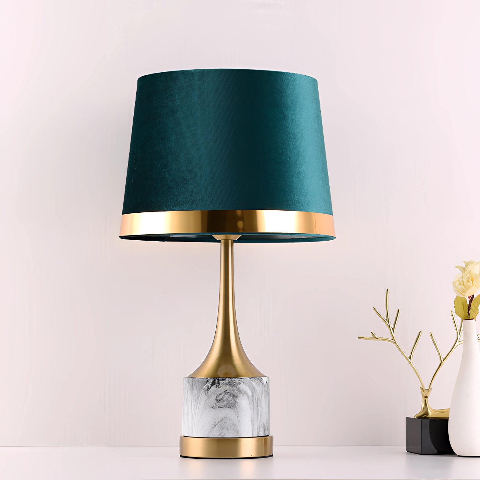 A modern luxury table lamp featuring a teal velvet lampshade with a gold base and marble accent, placed next to a green plant on a wooden surface, showcasing a stylish interior design element.