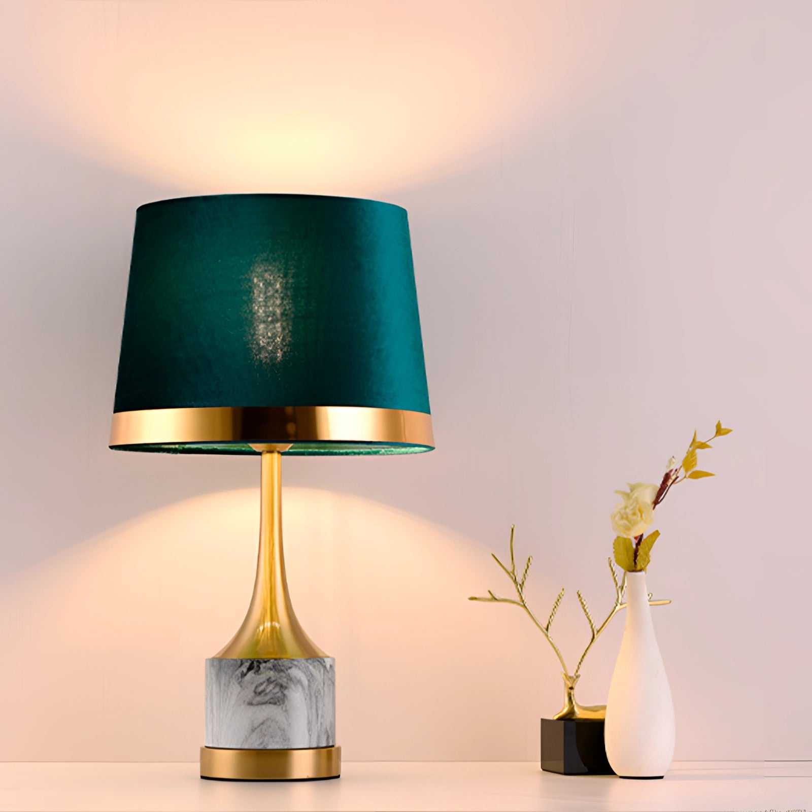 A modern luxury table lamp with a teal velvet shade, a sleek gold base, and a marble accent, displayed in a stylish room setting alongside a decorative plant and a vase.