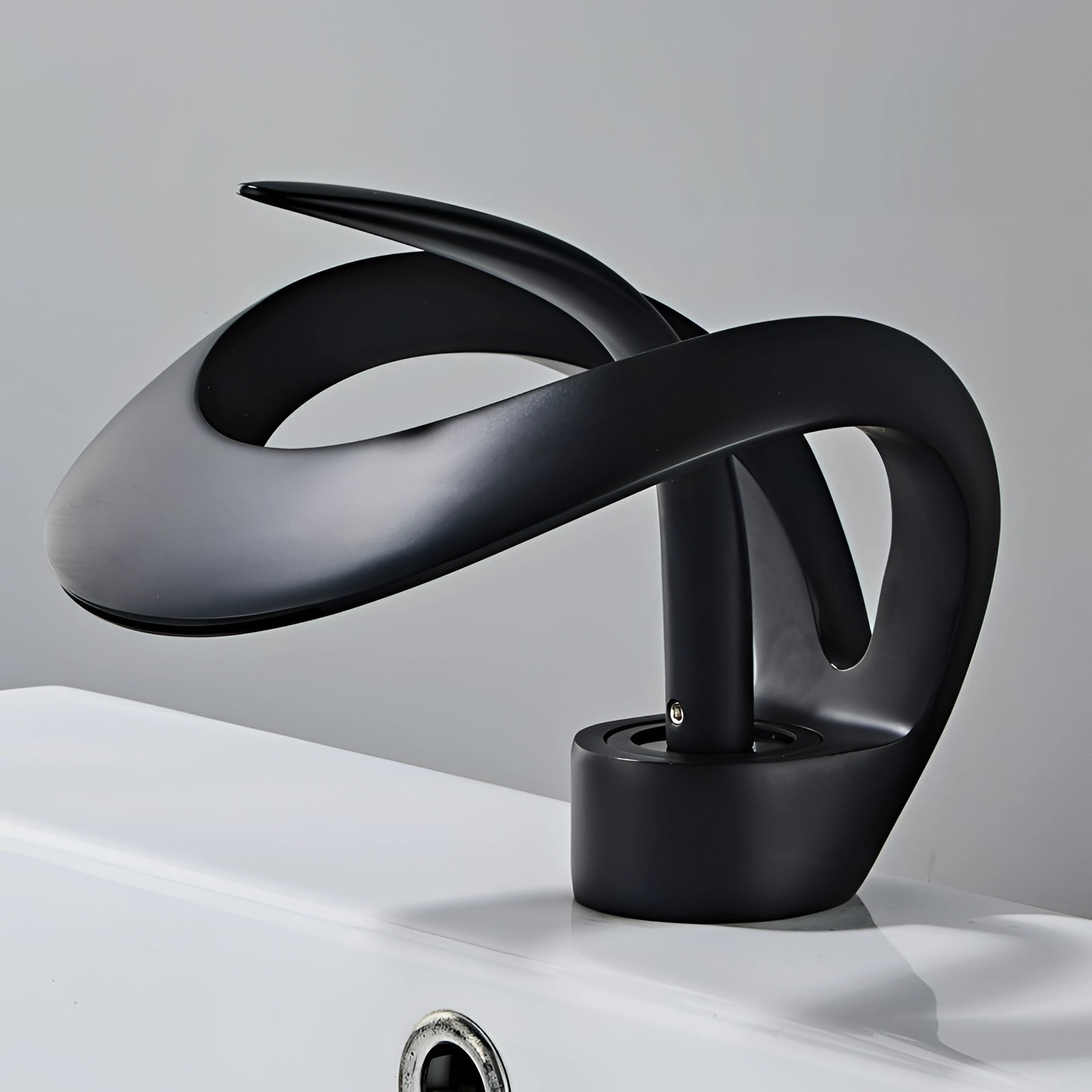 A sleek modern matte black waterfall faucet installed in a contemporary bathroom, showcasing a luxurious and futuristic design with a smooth curved spout above a white sink.