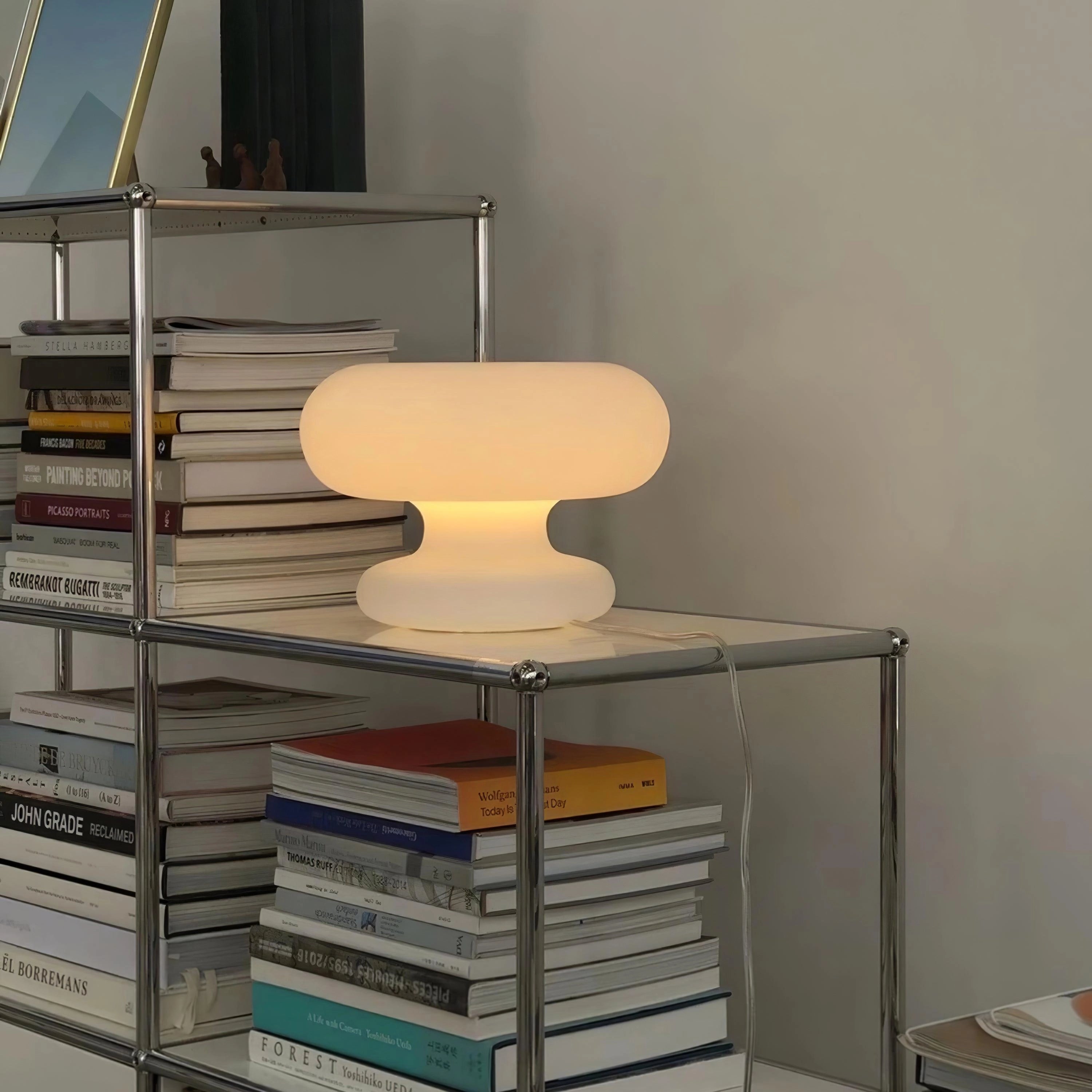 Modern mushroom table lamp with minimalist design on a wooden shelf next to books and decorative items.