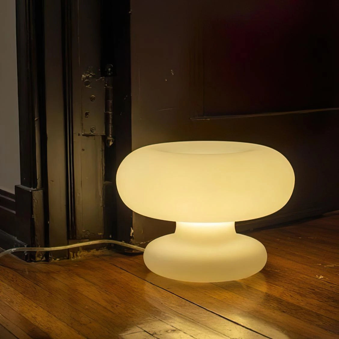 Modern mushroom-shaped table lamp with a minimalist design, placed on a wooden bedside table with hardwood flooring in the background.