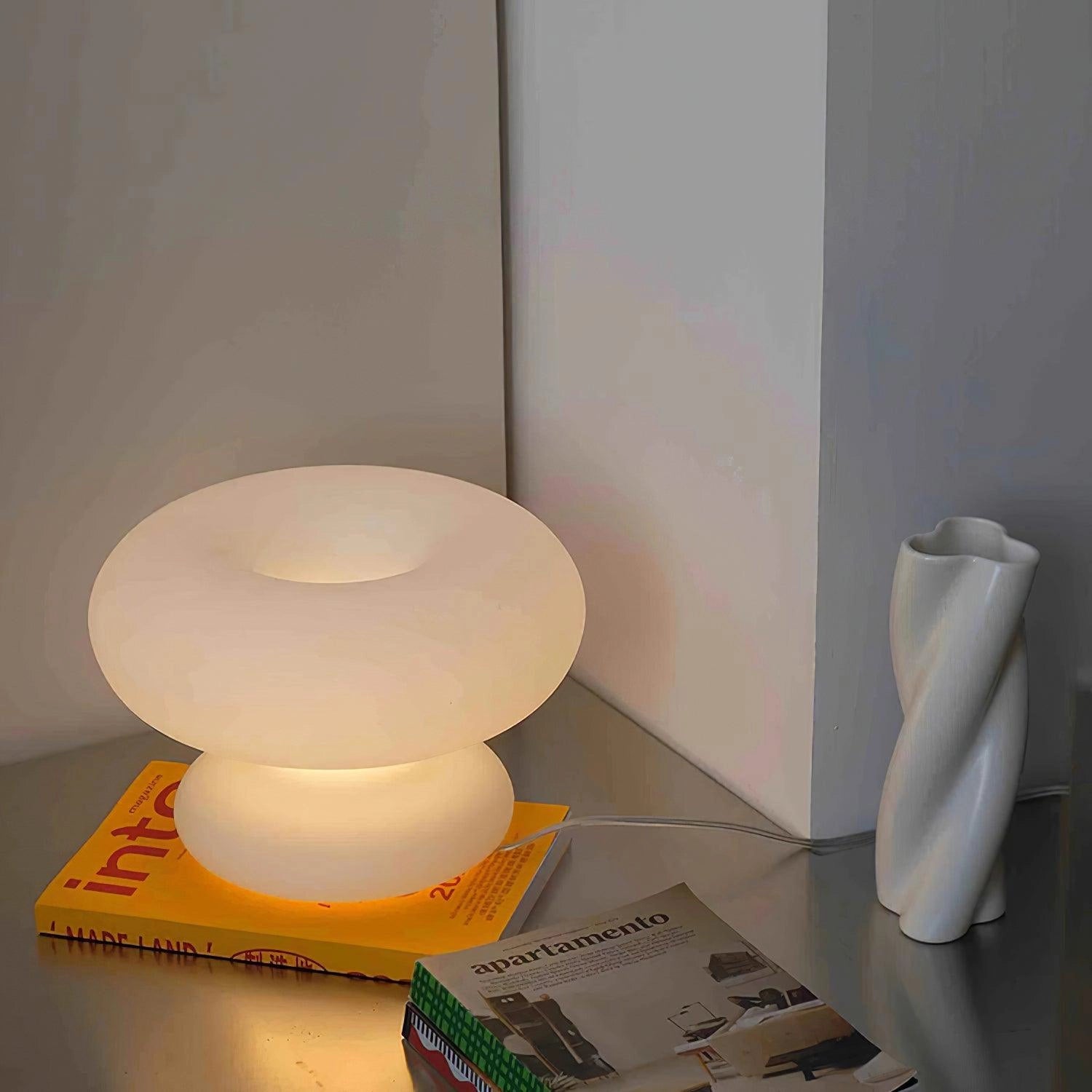 Modern mushroom-shaped table lamp with minimalist design, placed on a wooden table in a stylishly decorated room.