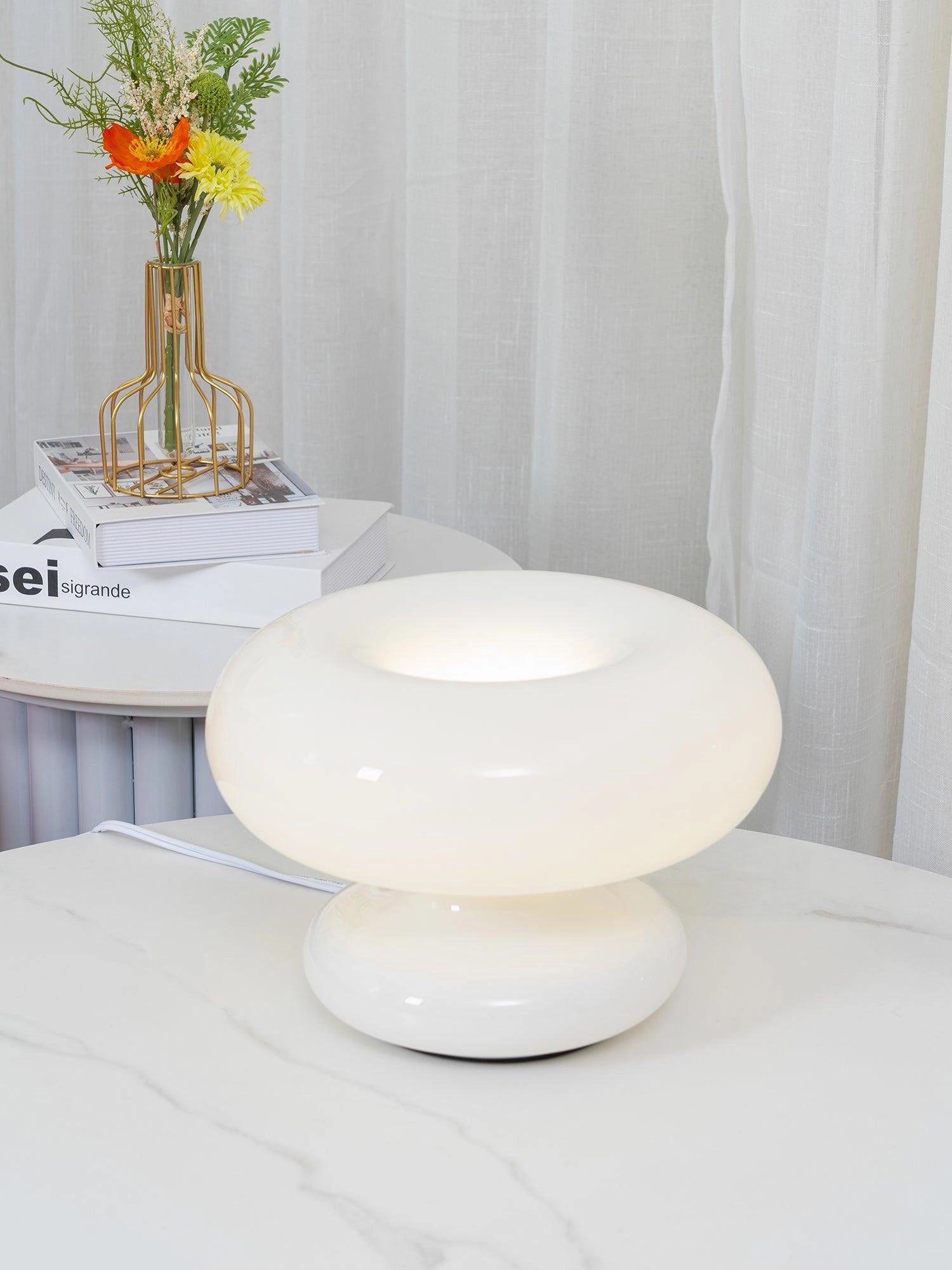 Modern mushroom table lamp on a wooden coffee table surrounded by minimalist dishware and a small flower vase, enhancing a contemporary interior design.