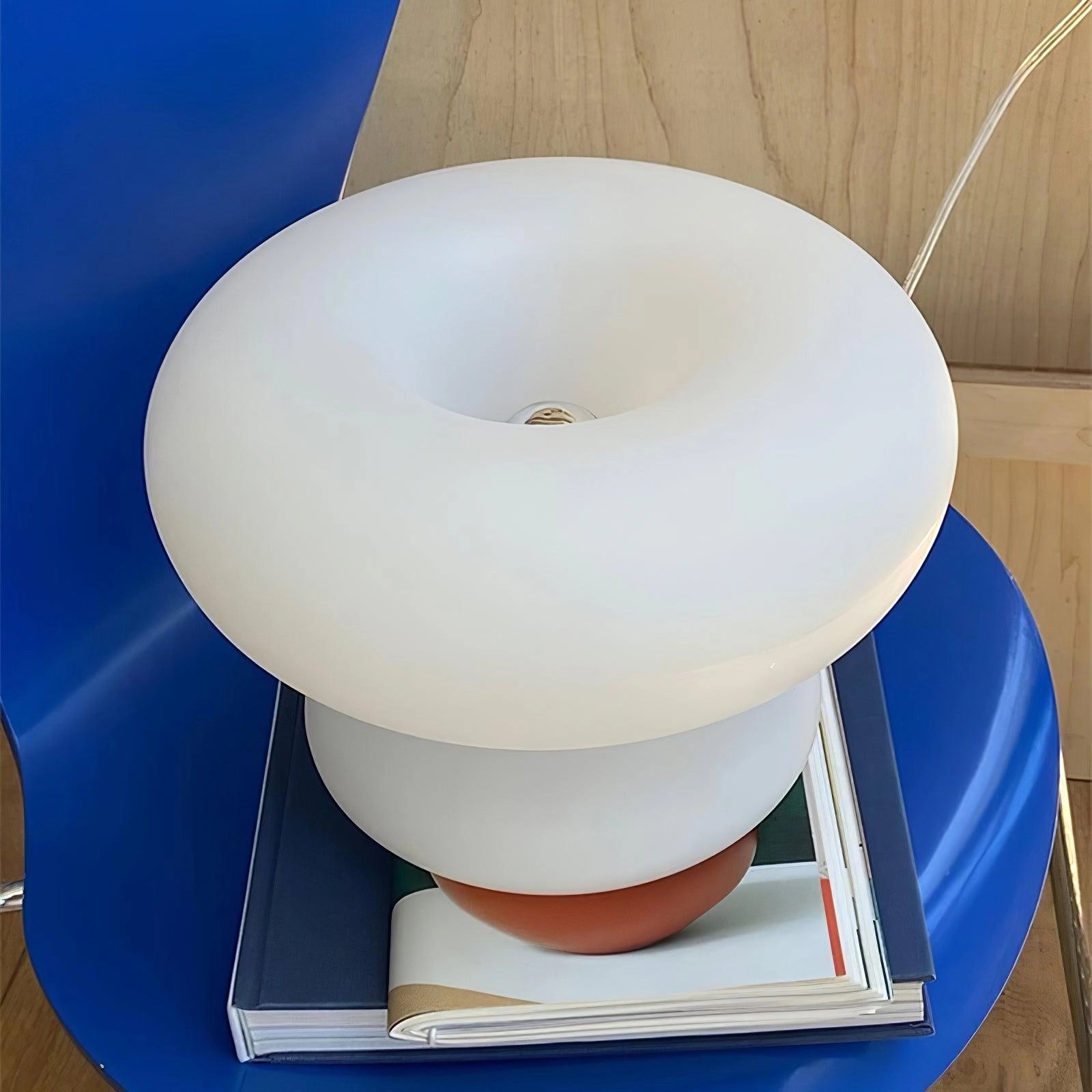 A modern mushroom-shaped table lamp with a minimalist design, featuring a blue light on a bedside table.