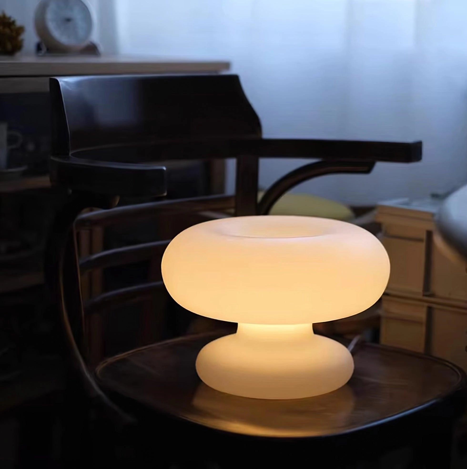 Modern mushroom-shaped table lamp with minimalist design, placed on a wooden table in a stylish interior setting featuring an office chair and coffee table.