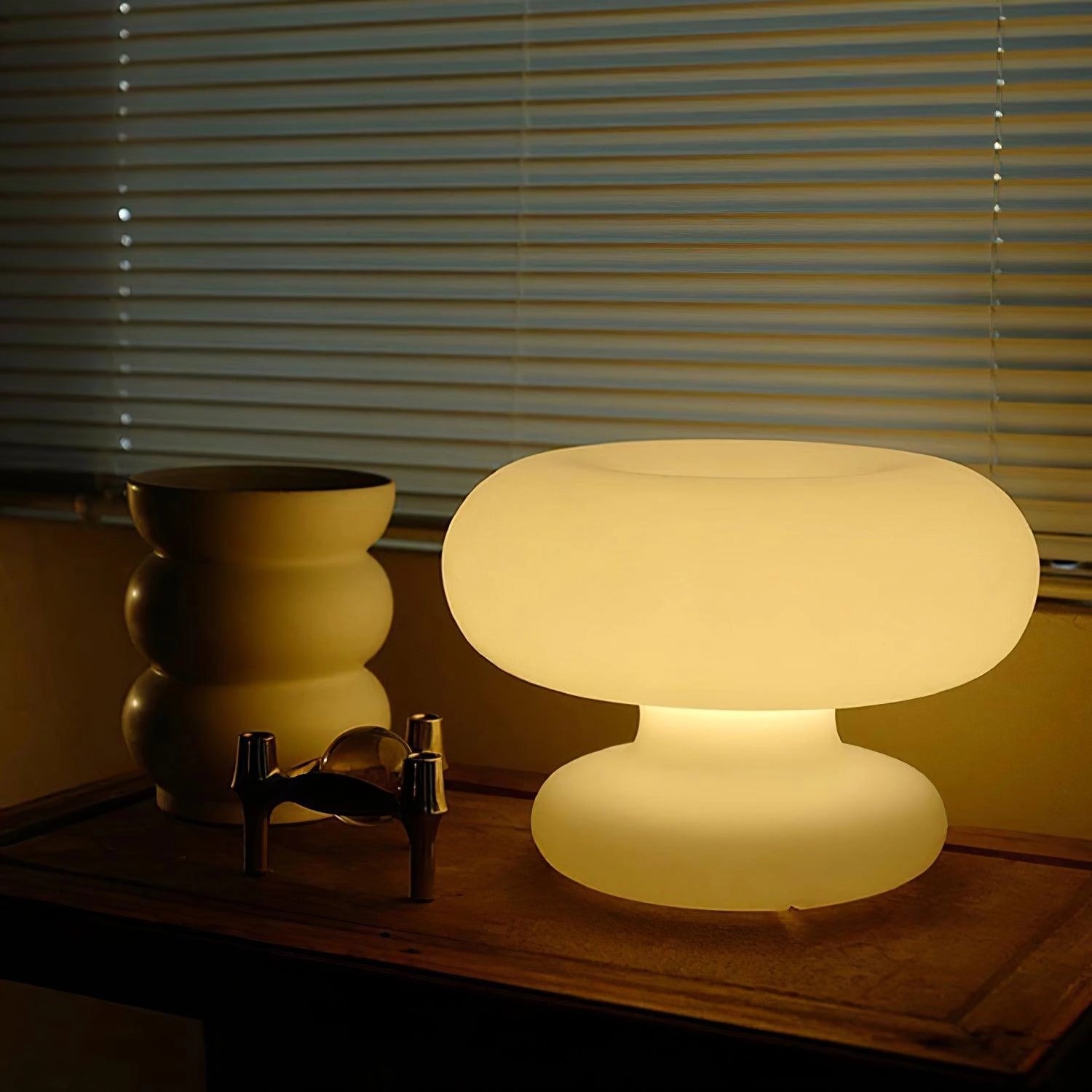 Modern minimalist mushroom-shaped table lamp with a wooden base and white shade, placed on a bedside table in a stylishly designed interior room.