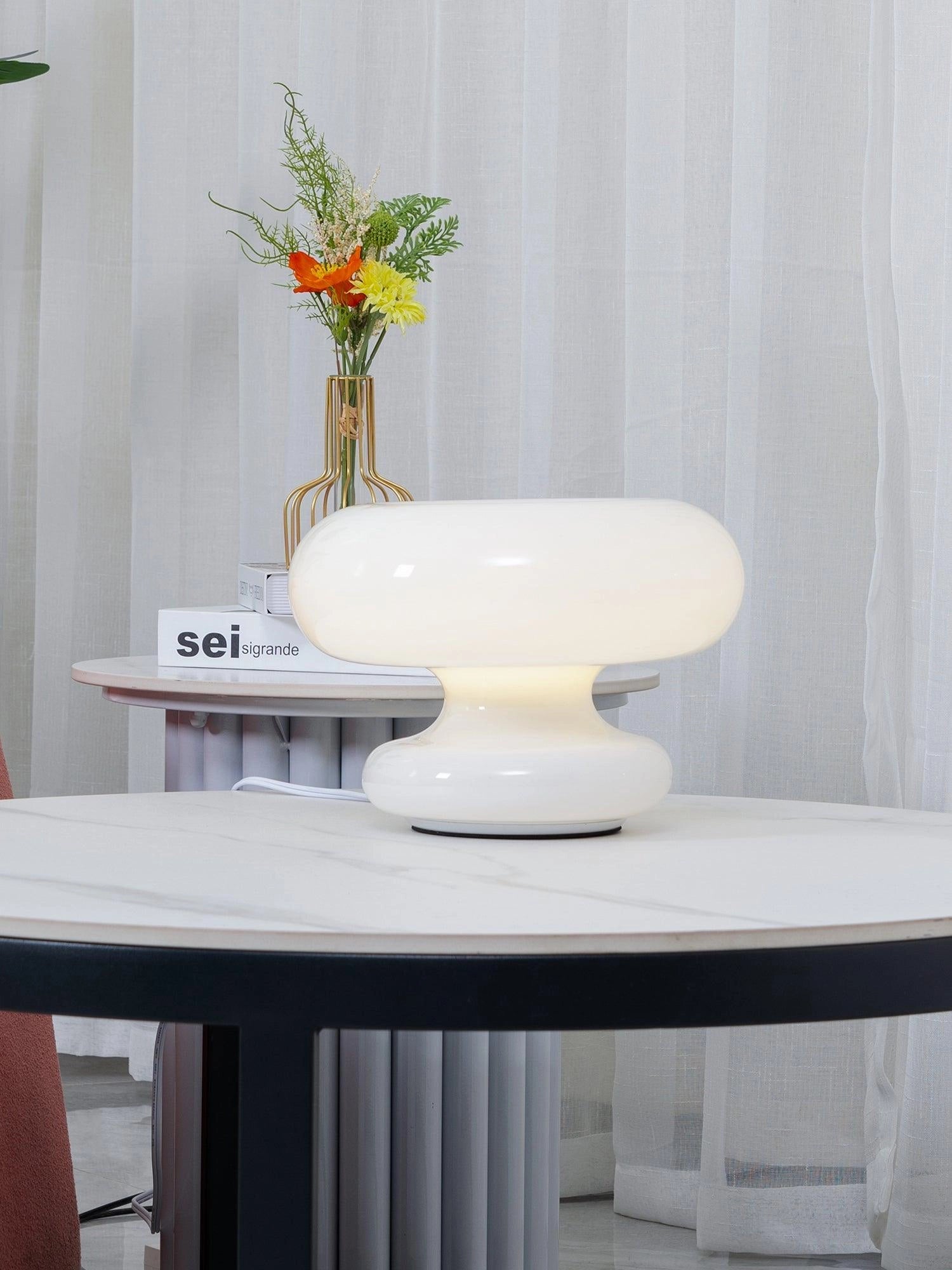 Minimalist modern mushroom table lamp with white shade on a bedside table, accompanied by a small plant and a vase, set against a stylish interior design with grey and purple accents.