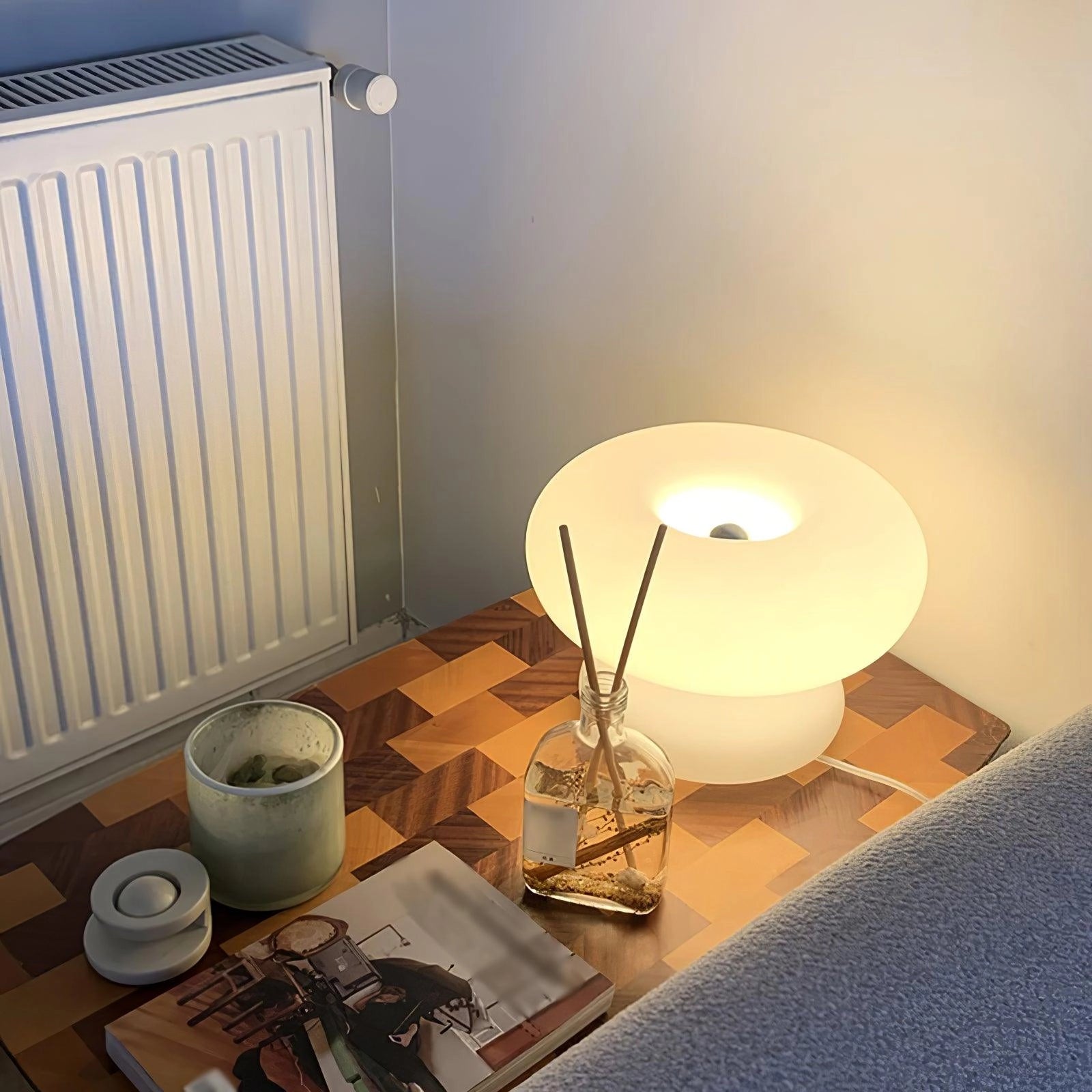 A minimalist modern mushroom table lamp on a wooden bedside table in a stylishly designed interior room with wooden flooring.