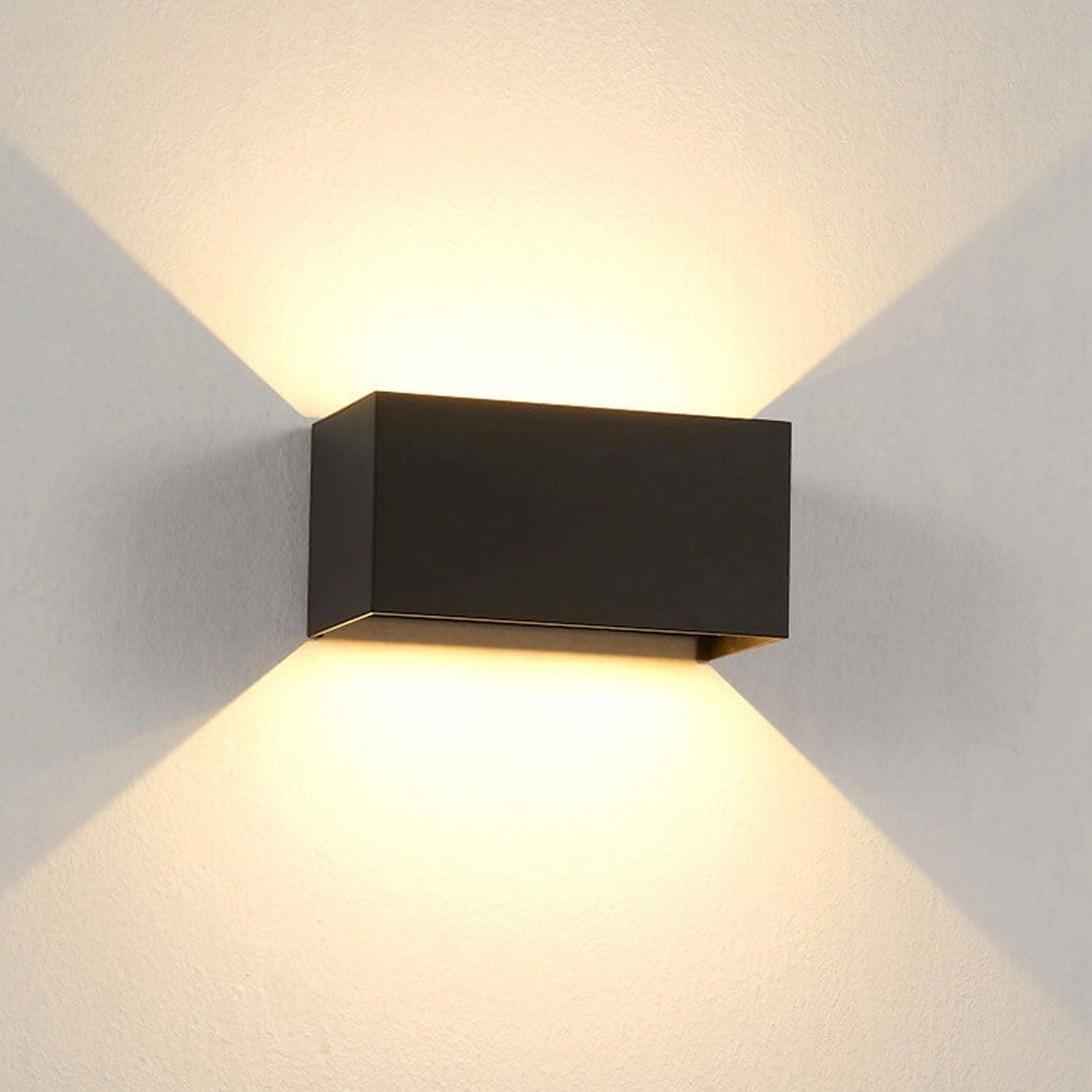 
A modern rectangular LED outdoor wall light in black with a warm light setting of 3000K, designed to be weather-resistant and suitable for USA/Canada voltage of 110 V-120 V. The light fixture is mounted on an exterior house wall, illuminating areas such as stairs or pathways.