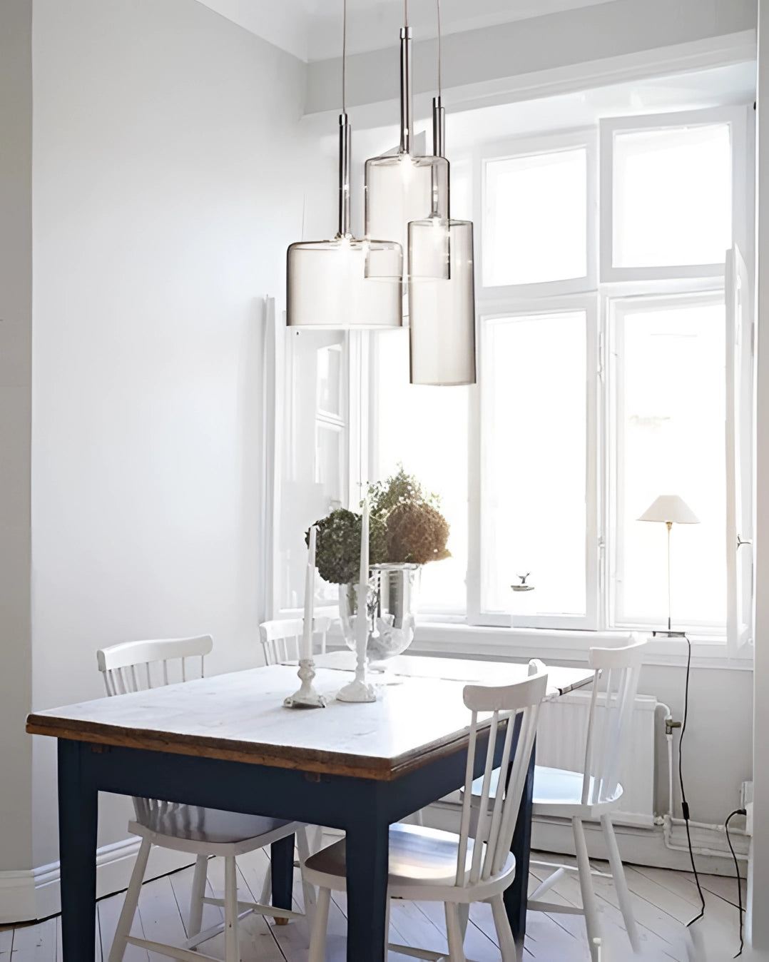 Modern Scandinavian glass pendant light hanging from the ceiling in a stylishly furnished room with a wooden table, chairs, and large windows, showcasing a contemporary grey and wood interior design.