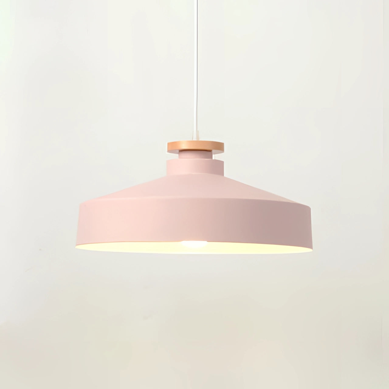 Modern Scandinavian pendant light with a pink disk-shaped shade and wooden accents hanging from a ceiling.