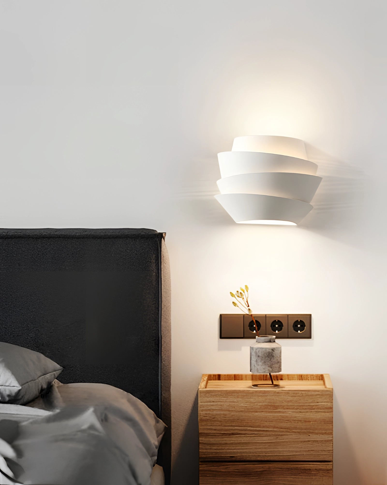 Modern sculptural LED pendant light with a minimalist spiral design hanging from the ceiling, illuminating a contemporary interior space with grey walls and wooden furniture, creating a stylish and comfortable ambiance.