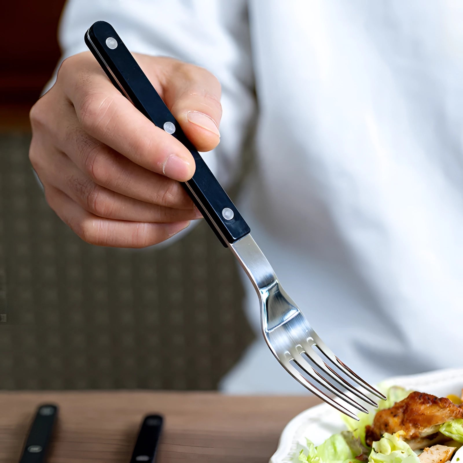 Modern stainless steel cutlery set with sleek black handles, consisting of 24 pieces including forks and other flatware, elegantly arranged alongside a plate in a dining setting.