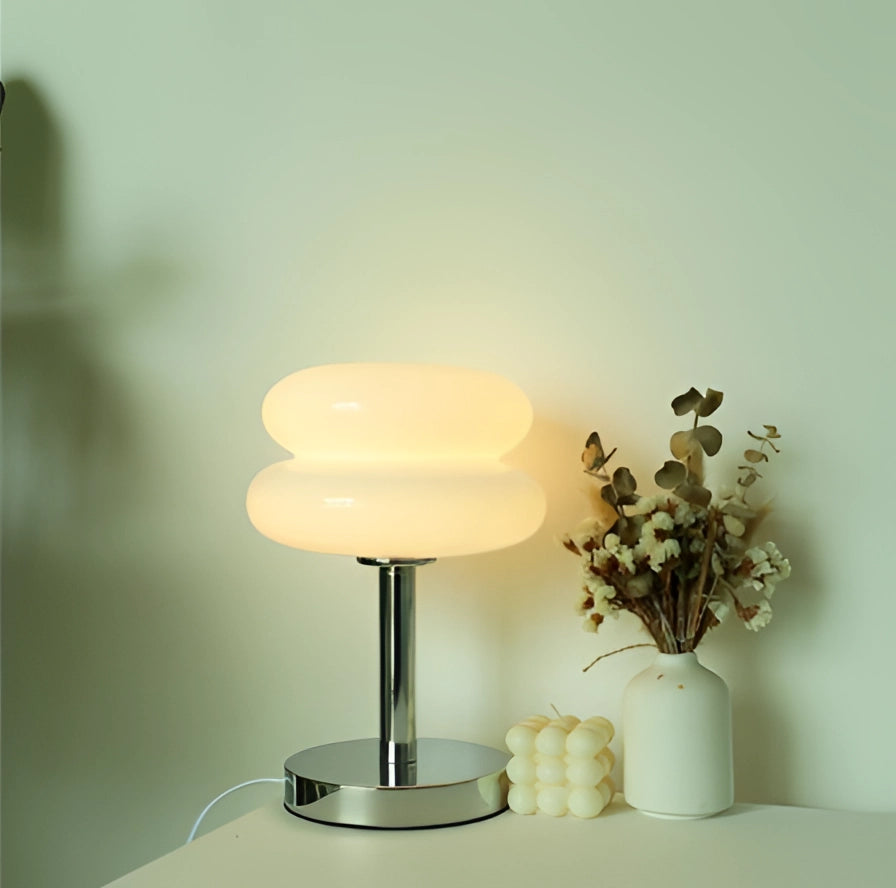 Modern tiered glass table lamp with a white thick bottom sits on a wooden table beside a small potted plant, showcasing its minimalist design and soft lampshade.