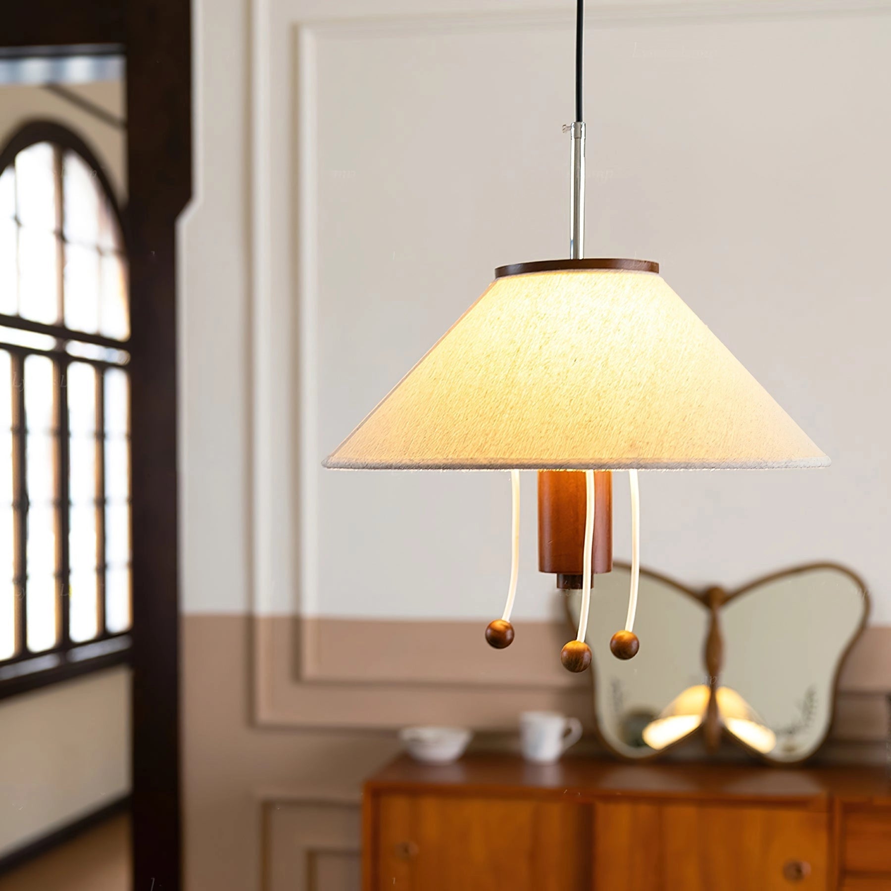 Modern triangle pendant lamp with wooden accents hanging in a stylish interior setting with natural light from a window, shelves, and other decor elements visible.