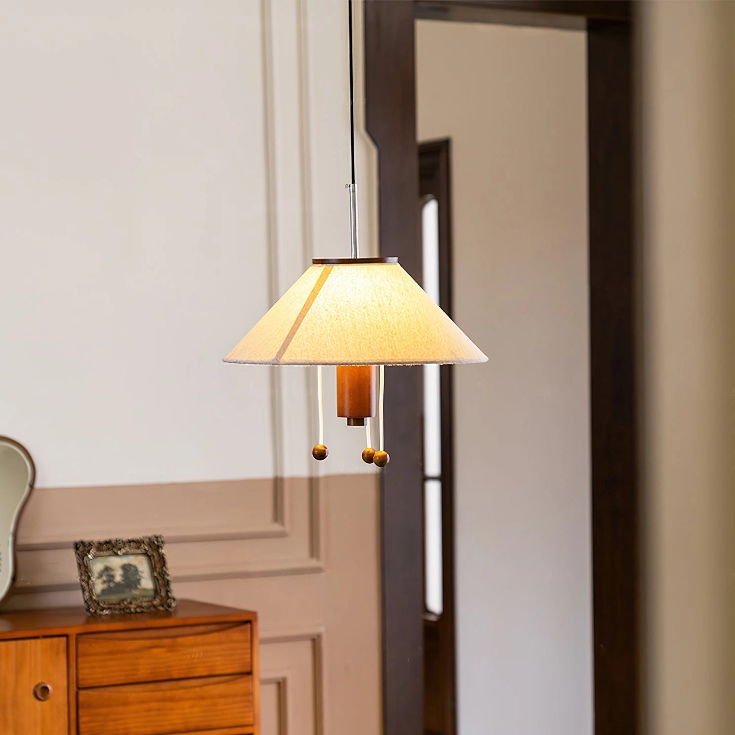 Modern triangle pendant lamp with wooden accents, featuring adjustable lighting, hanging above a wooden dresser with shelving and cabinetry in the background.