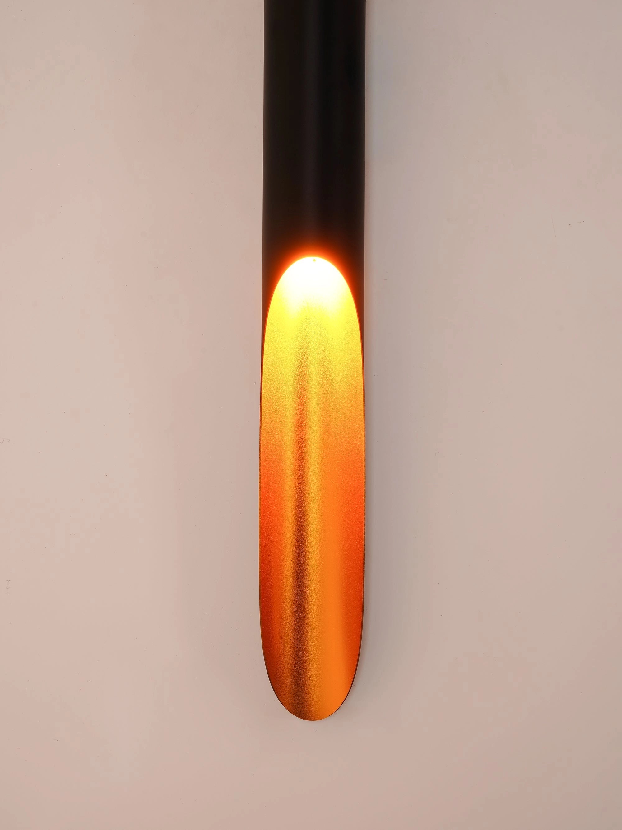 A modern vertical LED wall sconce with a minimalist design, featuring an amber-tinted cylindrical glass shade that emits a warm glow, suitable for architectural lighting.