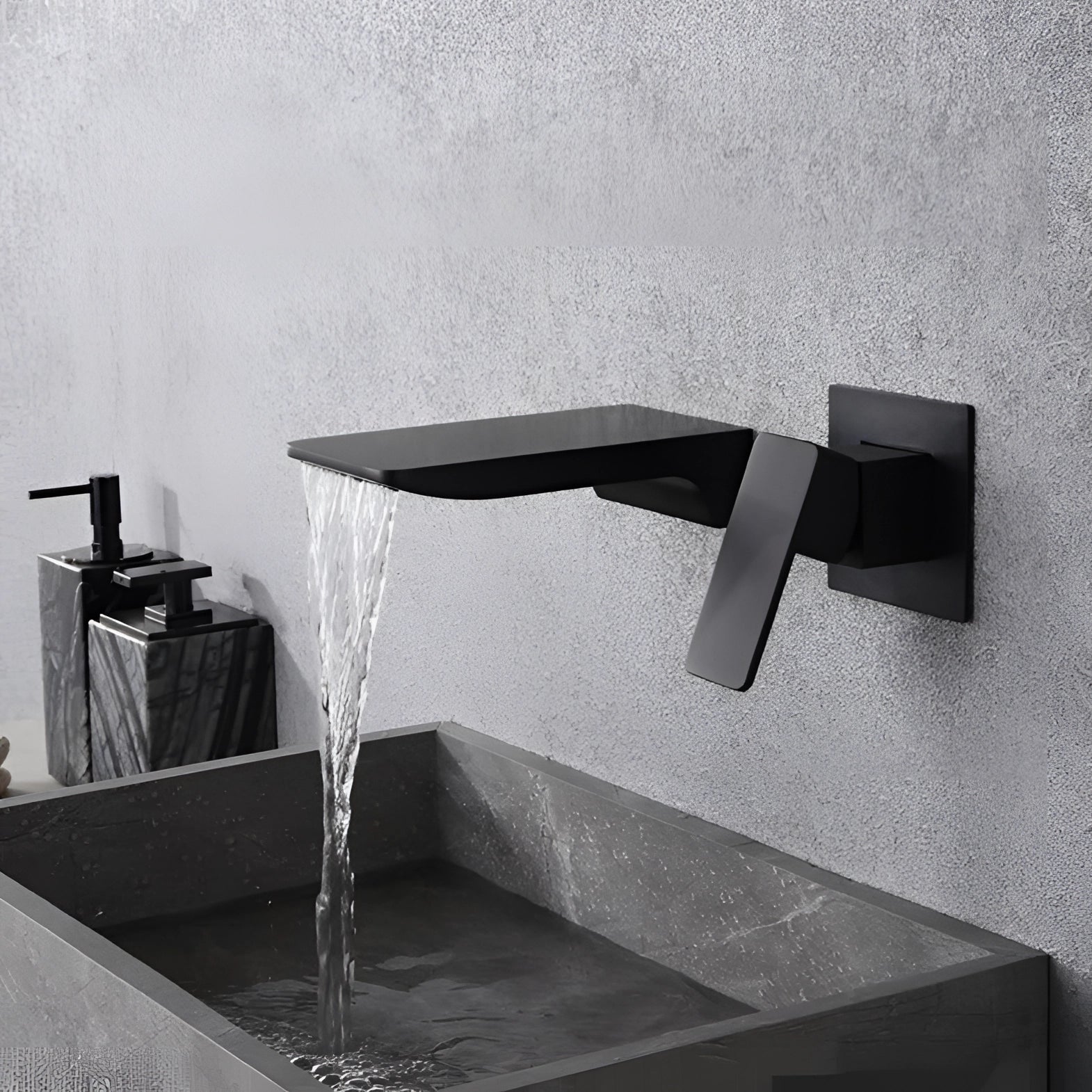 Sleek black wall-mounted waterfall faucet with a modern square design and chrome finish, set against a backdrop of grey and wood textures.