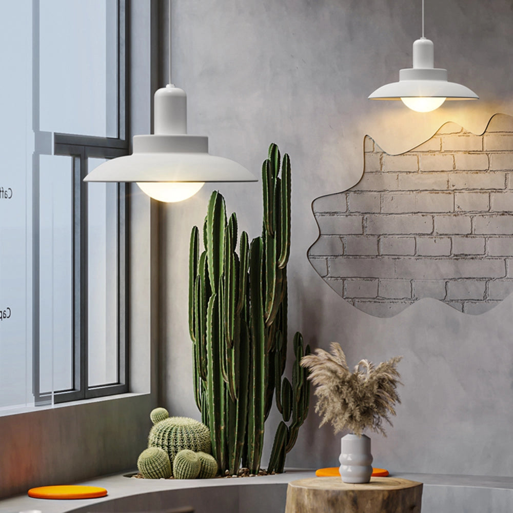 Modern white pendant light hanging above a wooden table, surrounded by minimalist interior design elements including a small potted plant. The lamp is adjustable and emits a warm glow, enhancing the contemporary aesthetic of the kitchen space.