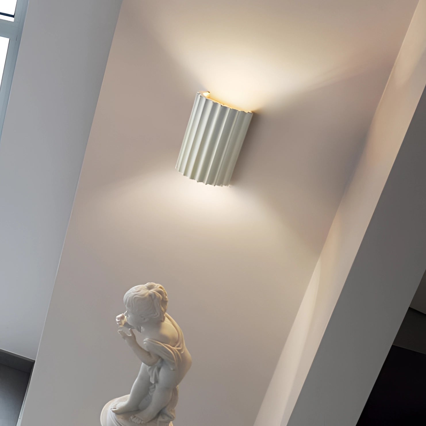 Modern white ribbed wall sconce mounted on a contemporary indoor setting with wooden stairs and flooring, highlighting the architectural design and artistic ambiance.