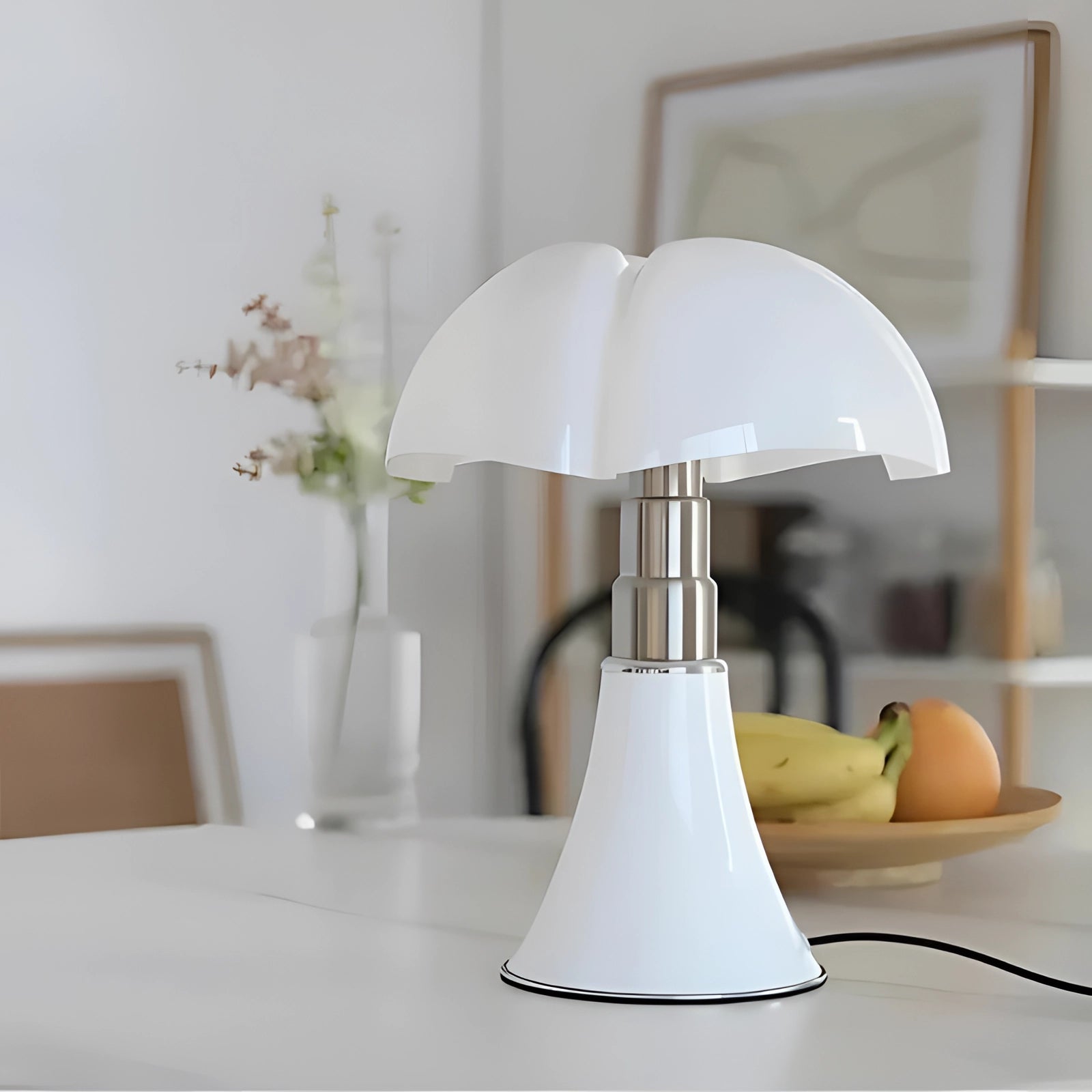 Modern white table lamp with a contemporary minimalist mushroom design, placed on a wooden desk next to a small potted plant, set in a stylish interior space.