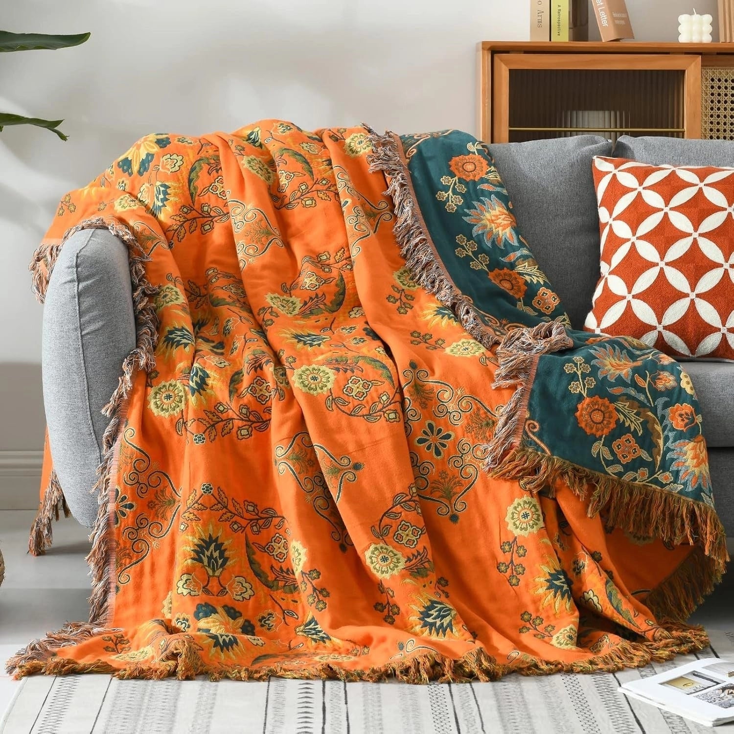 Orange paisley bohemian tassel throw blanket with intricate patterns, made of luxury cotton, draped elegantly over a wooden surface.