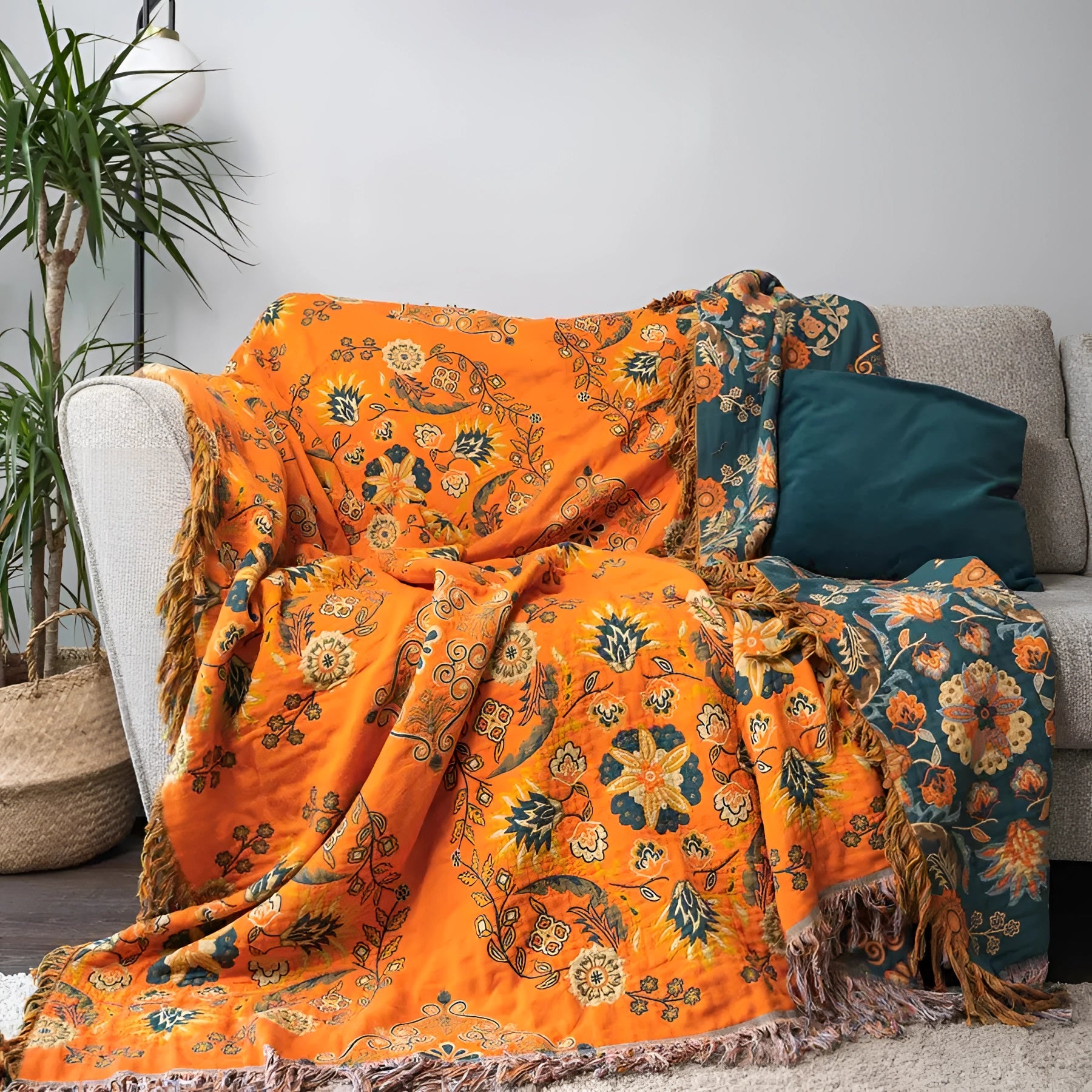 Orange paisley bohemian tassel throw blanket draped over a surface, showcasing its luxurious cotton fabric and intricate pattern, with a nearby flowerpot containing a houseplant adding to the decor.