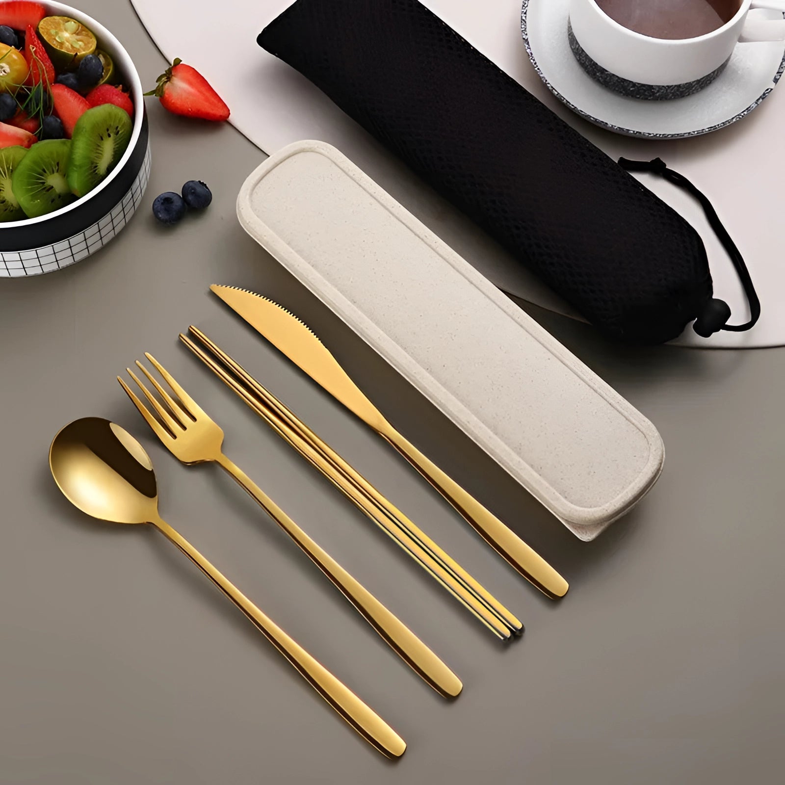 Portable eco-friendly stainless steel travel cutlery set in gold color displayed on a table, including a fork, knife, spoon, and chopsticks, all arranged neatly alongside a matching rectangular carrying case.