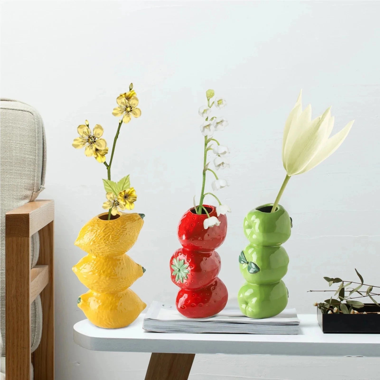 Red ceramic strawberry-shaped vase filled with artificial flowers, displayed on a table, showcasing a unique fruit-themed home decor piece.