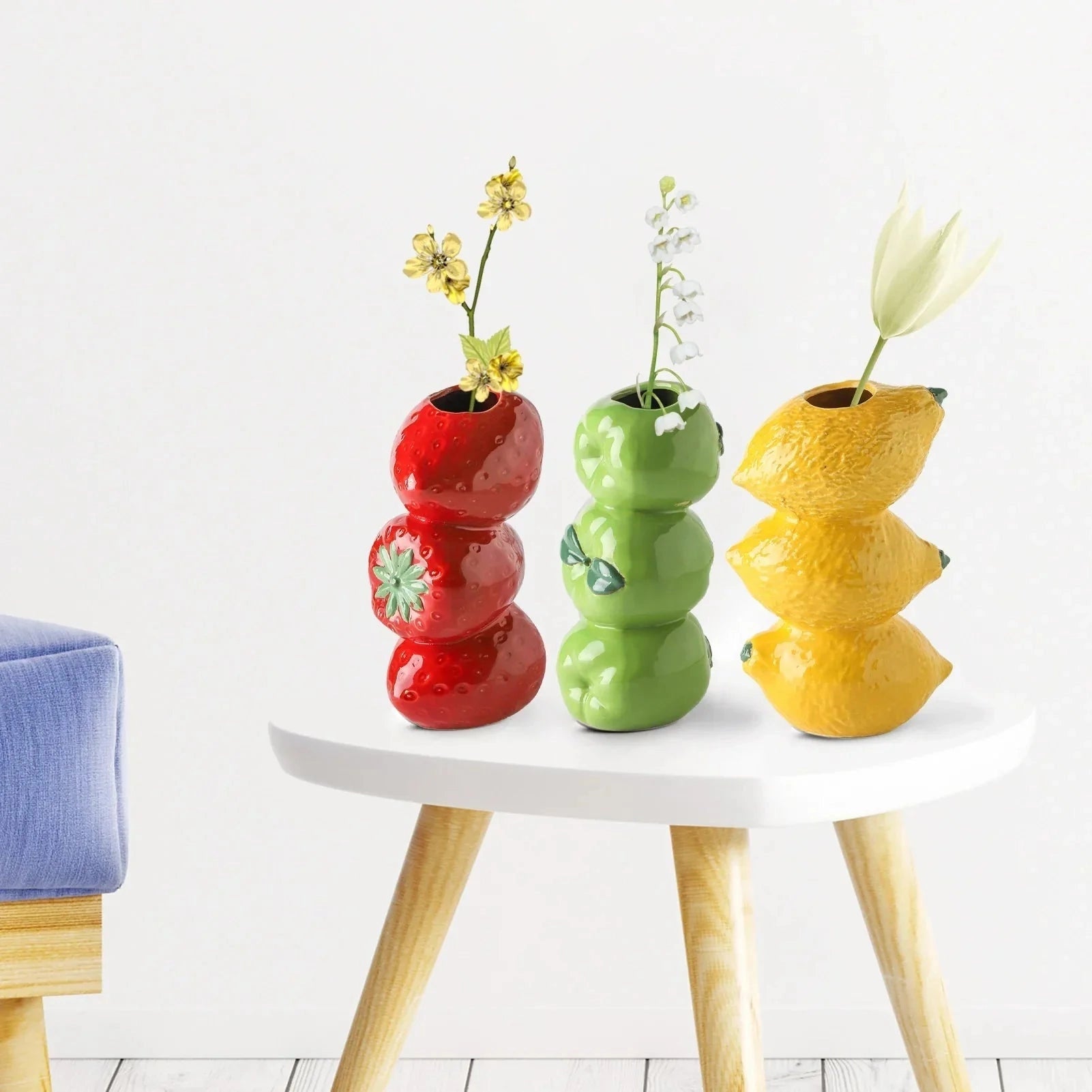 Red ceramic vase shaped like a strawberry, placed on a table surrounded by furniture, used as a decorative piece for home interiors.