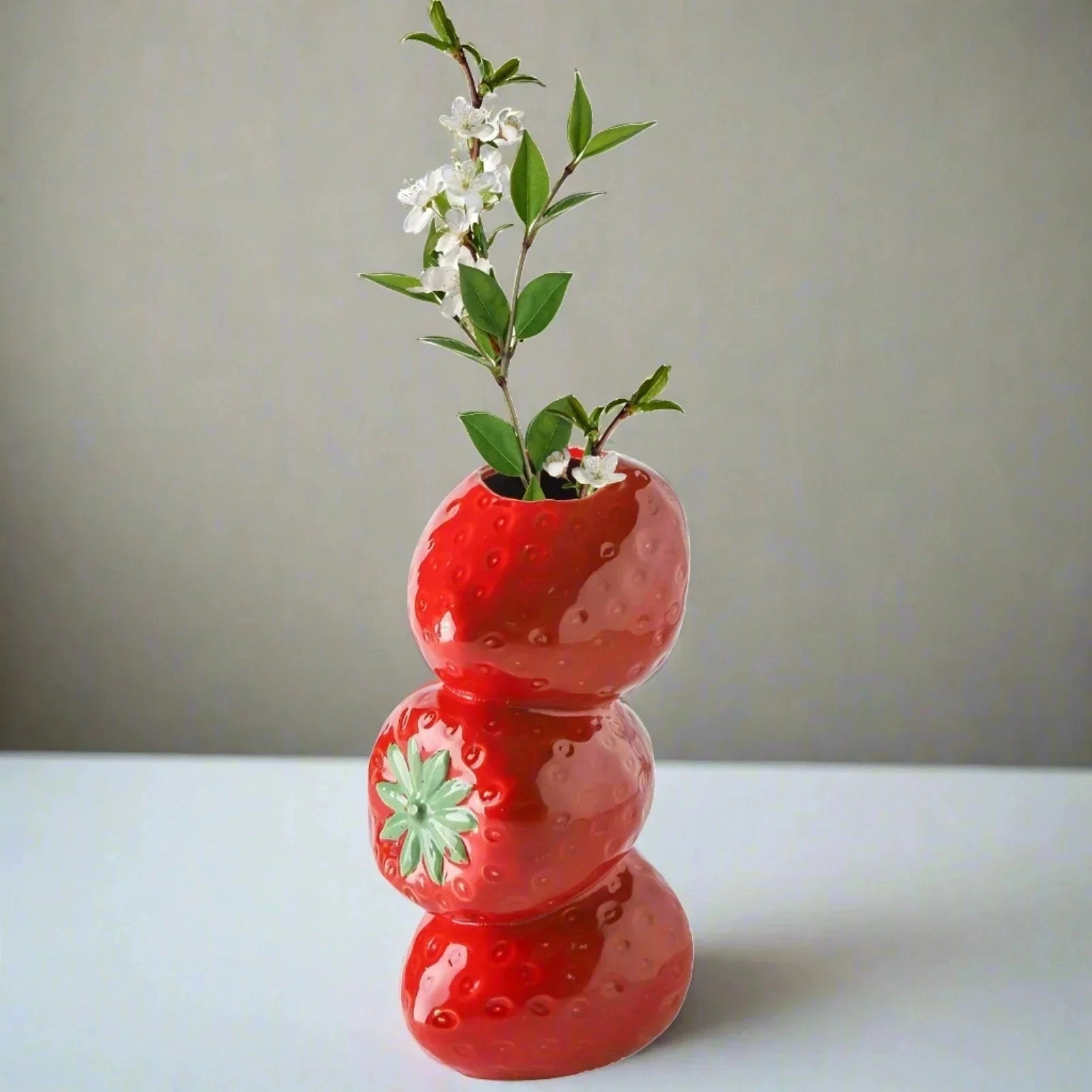 Red ceramic strawberry-shaped vase with intricate detailing, filled with vibrant artificial flowers, ideal for adding a touch of whimsical, fruit-themed decor to any space.