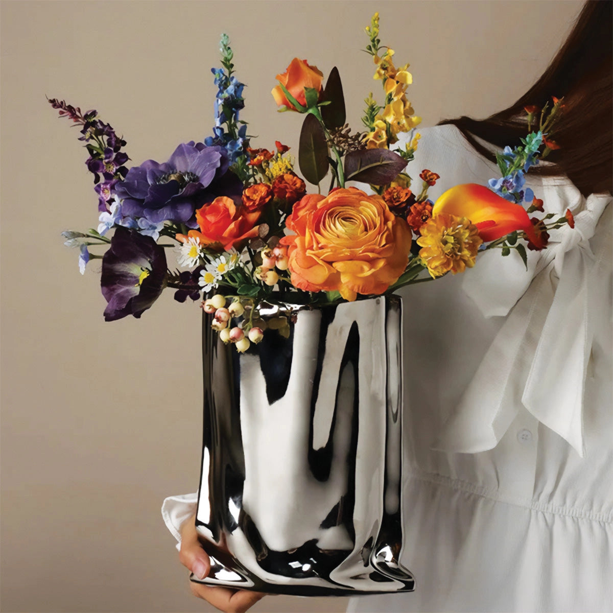 Reflective chrome vase with a high gloss finish, featuring a modern design and filled with an elegant arrangement of artificial roses and other flowers.