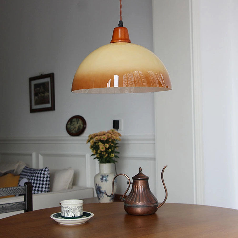 A retro yellow mid-century pendant light hanging above a wooden table adorned with tableware, a potted plant, and a picture frame, enhancing the modern home decor.