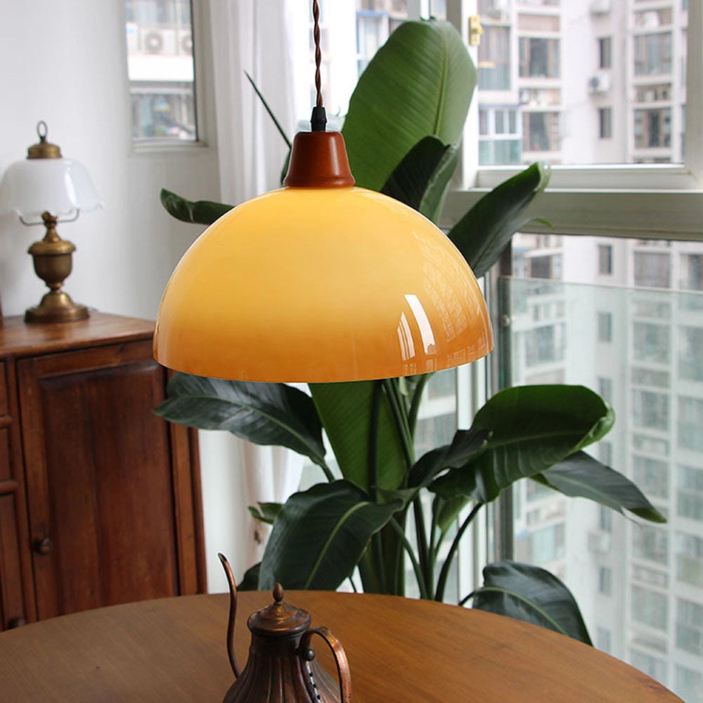 A retro yellow mid-century pendant light hanging above a wooden table with a potted plant, surrounded by modern home decor including chairs and large windows.