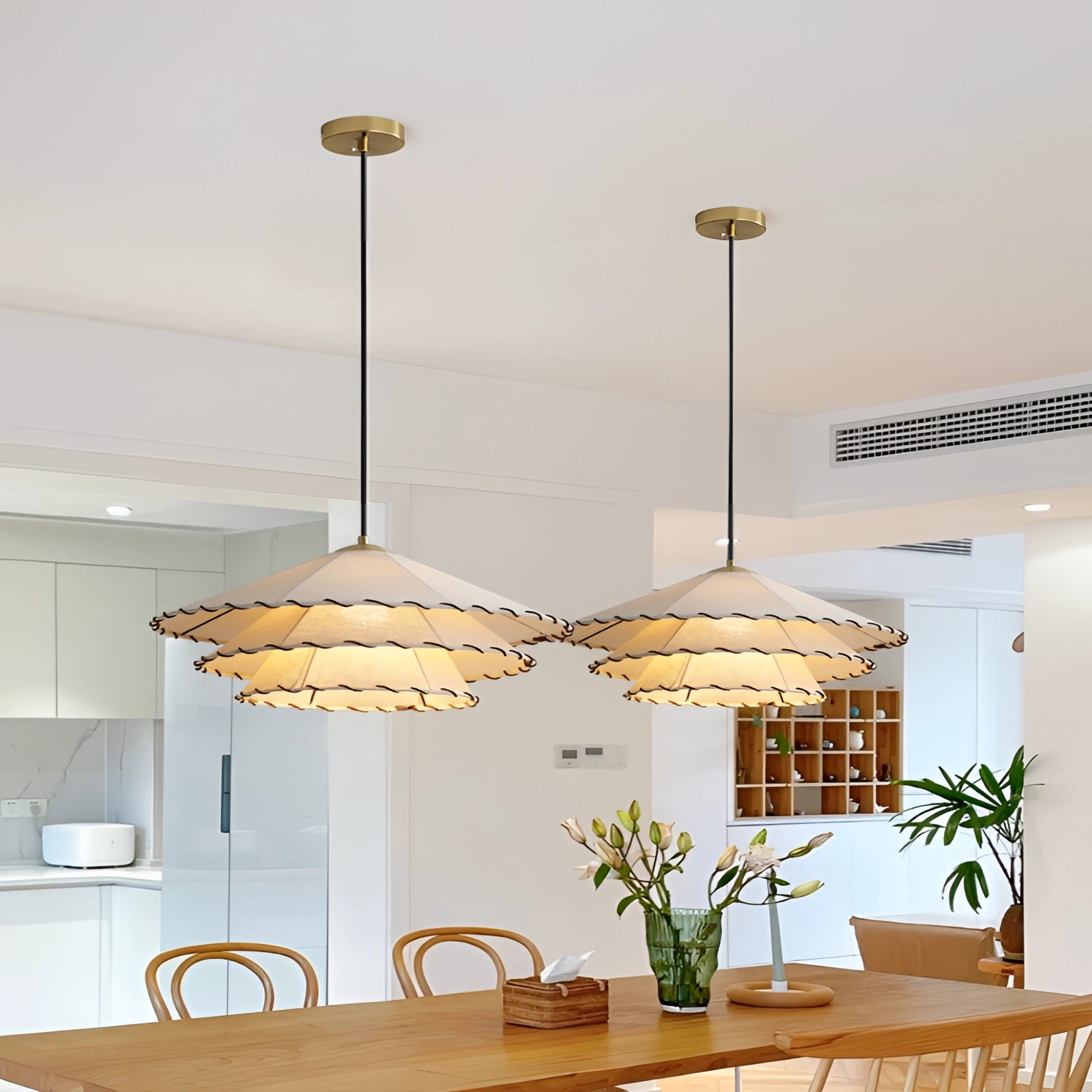 Modern tiered chandelier with scalloped LED pendant light featuring a gold interior, hanging above a wooden table with a houseplant in a flowerpot nearby.