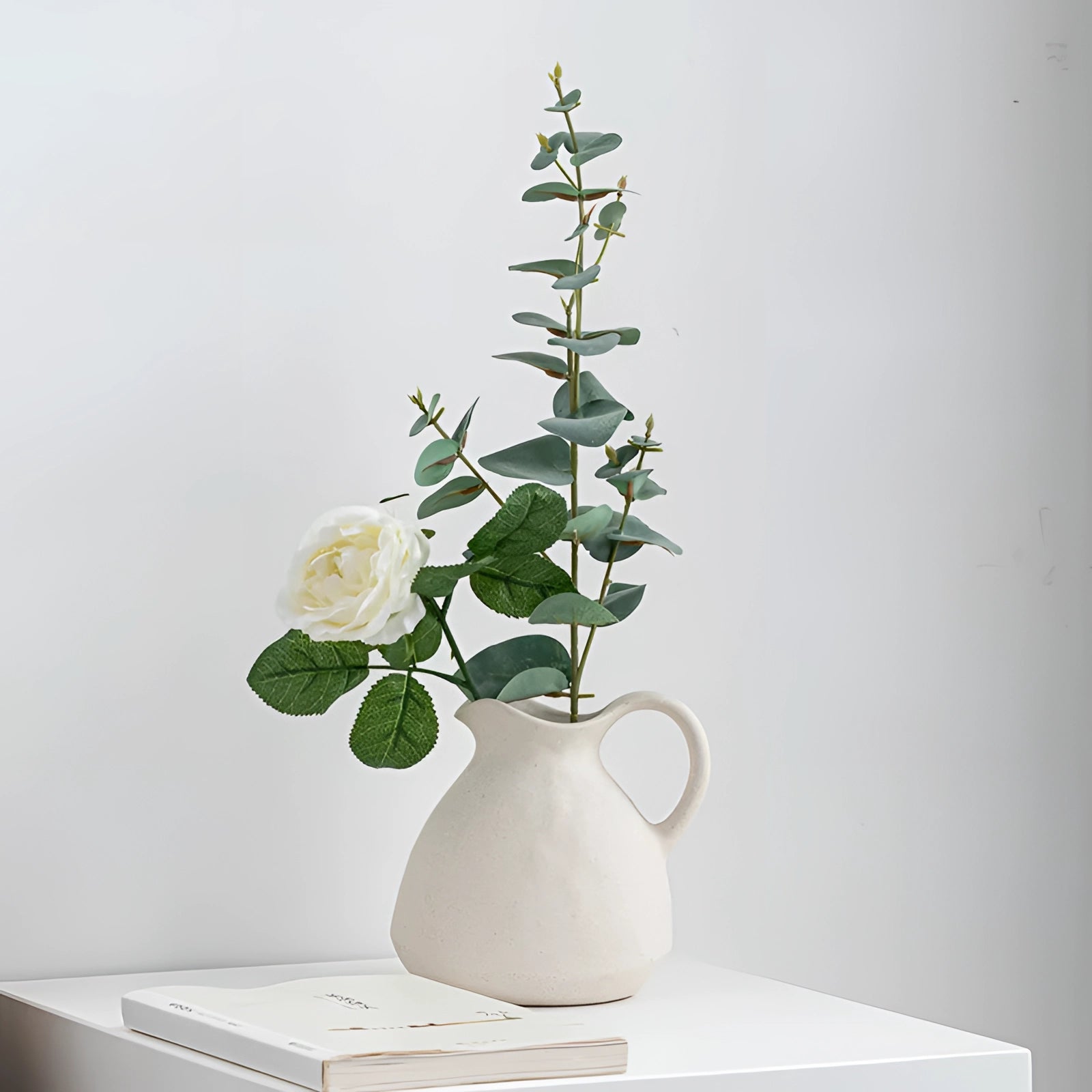 Scandinavian ceramic flower jug with a minimalist design in white, featuring a simple and elegant vase filled with a variety of flowering plants and twigs, ideal for home decor.