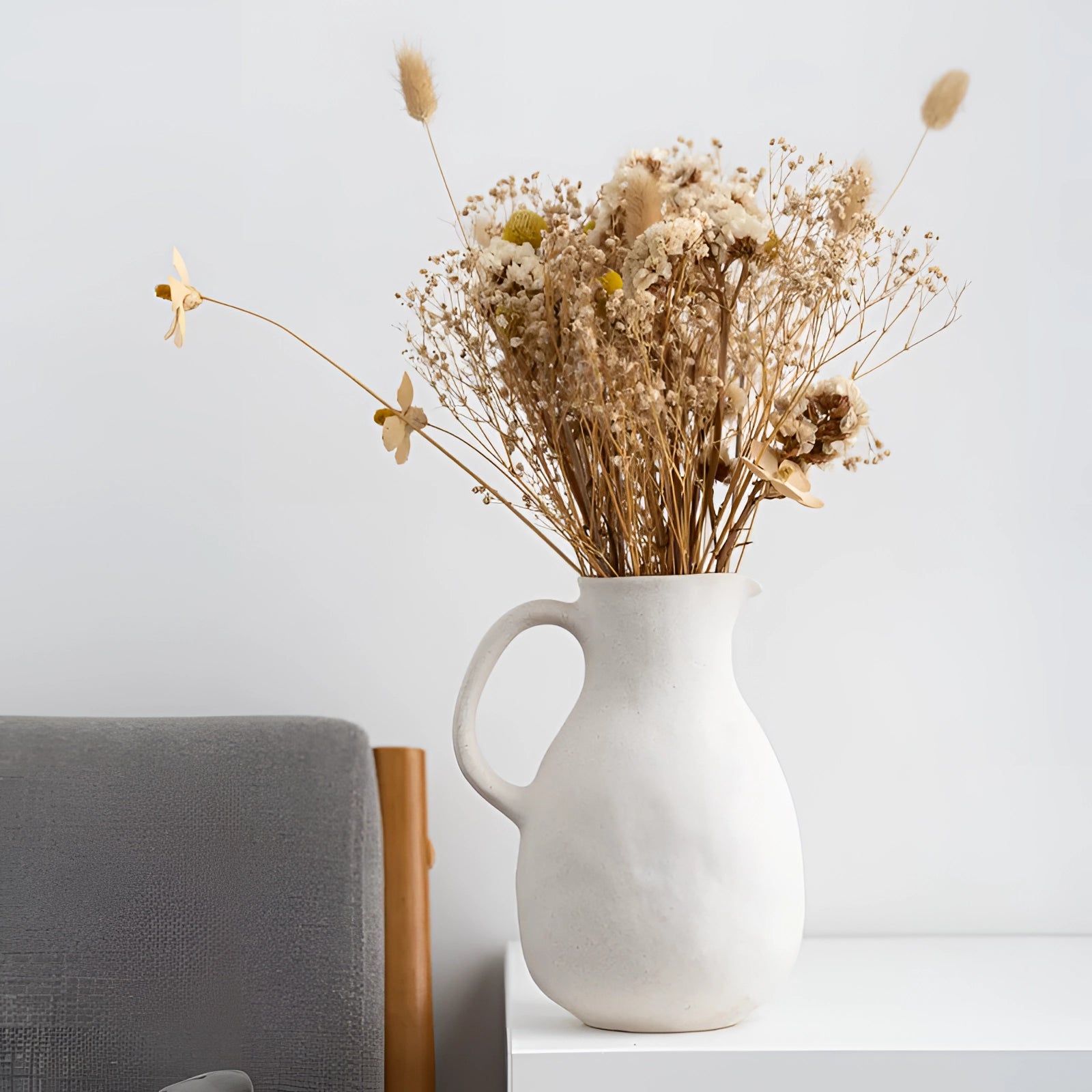 Minimalist white ceramic jug vase with delicate floral arrangement, featuring twigs and branches, showcasing Scandinavian design aesthetics.