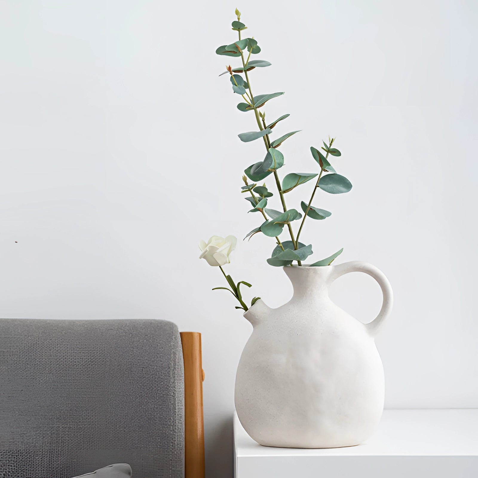 Minimalist white Scandinavian ceramic flower jug used as a vase, elegantly displaying a variety of flowers and greenery, showcasing its artistic and decorative function in home decor.